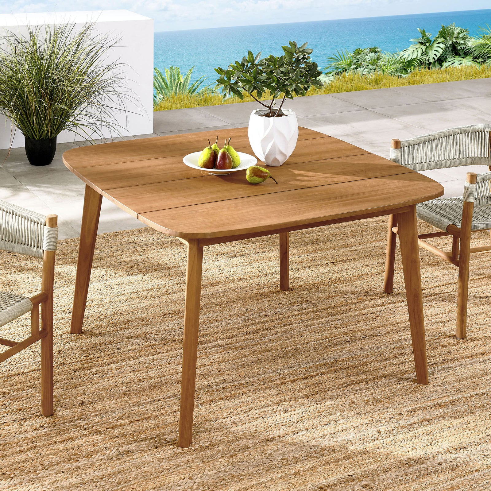 Vienna 46 inch natural teak patio table arranged with chairs and decor for relaxed outdoor dining by the water. || EEI-6815-NAT || front_angle_room