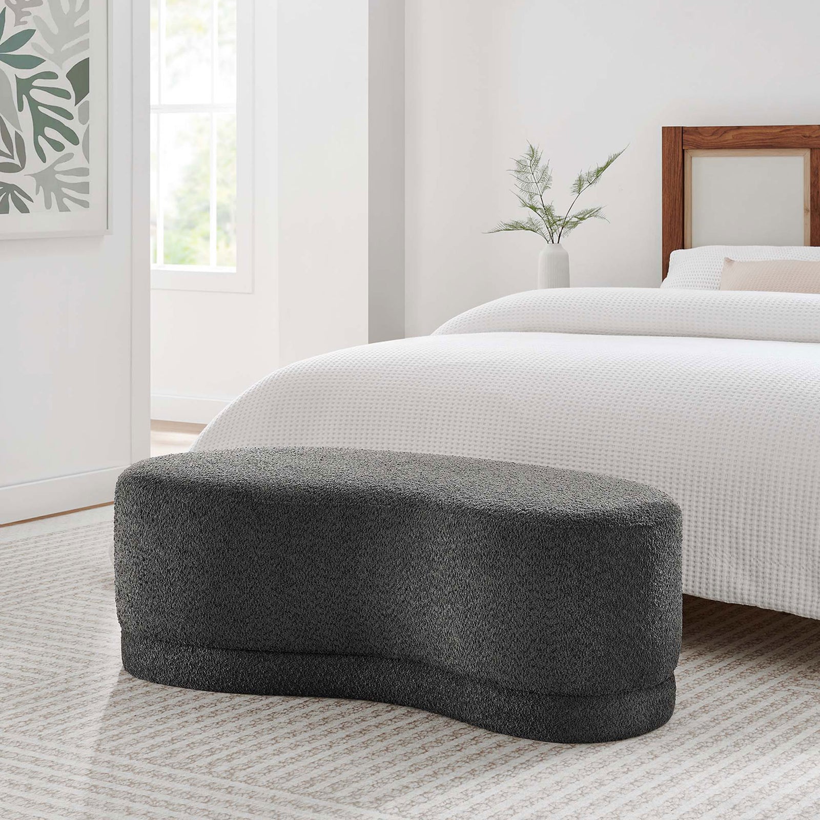 Curved dark gray upholstered ottoman bench styled at the foot of a bed for added seating and softness. || EEI-6816-SLA || front_angle_room