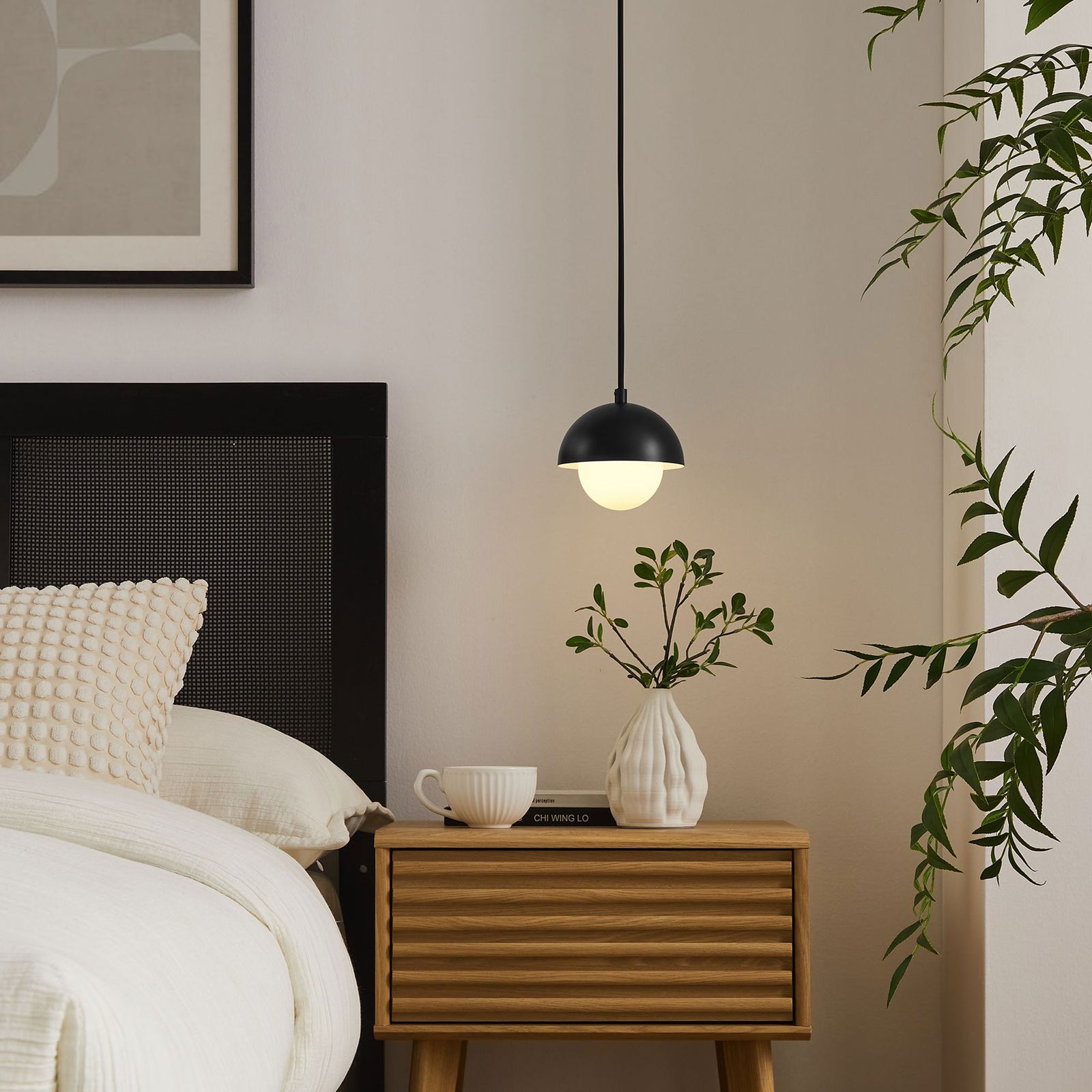 Glowing black globe pendant casting warm light over a bedside table for soft nighttime illumination || EEI-6870-BLK || front_on_room