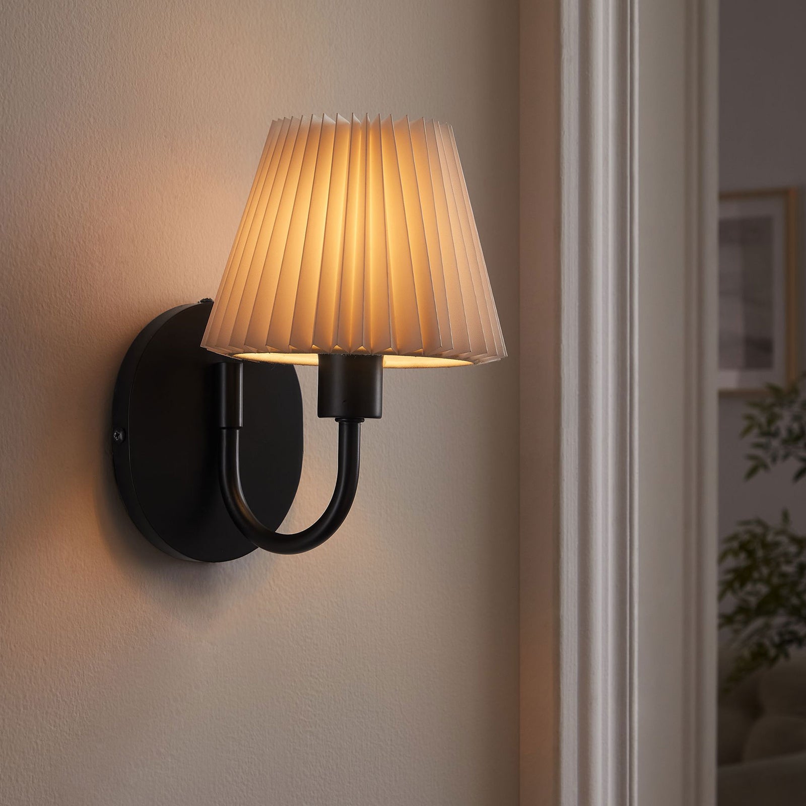 Lit black U-shaped wall sconce with pleated shade casts a cozy glow, framing a doorway in the living room. || EEI-6872-BLK || front_angle_on_room
