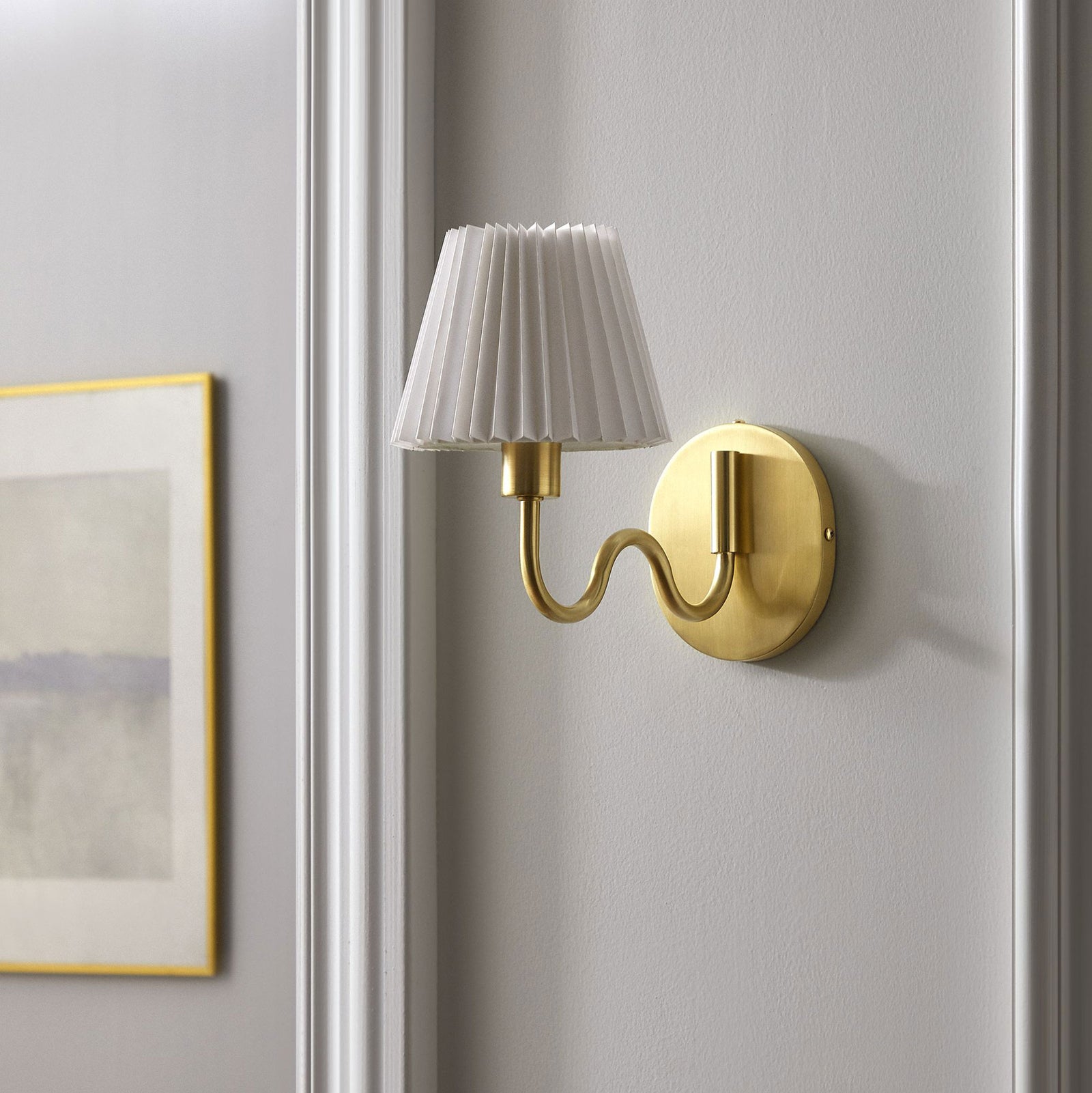 Brass squiggle arm sconce with pleated shade brings a touch of glam warmth to a clean, neutral hallway wall. || EEI-6873-BRA || front_angle_room