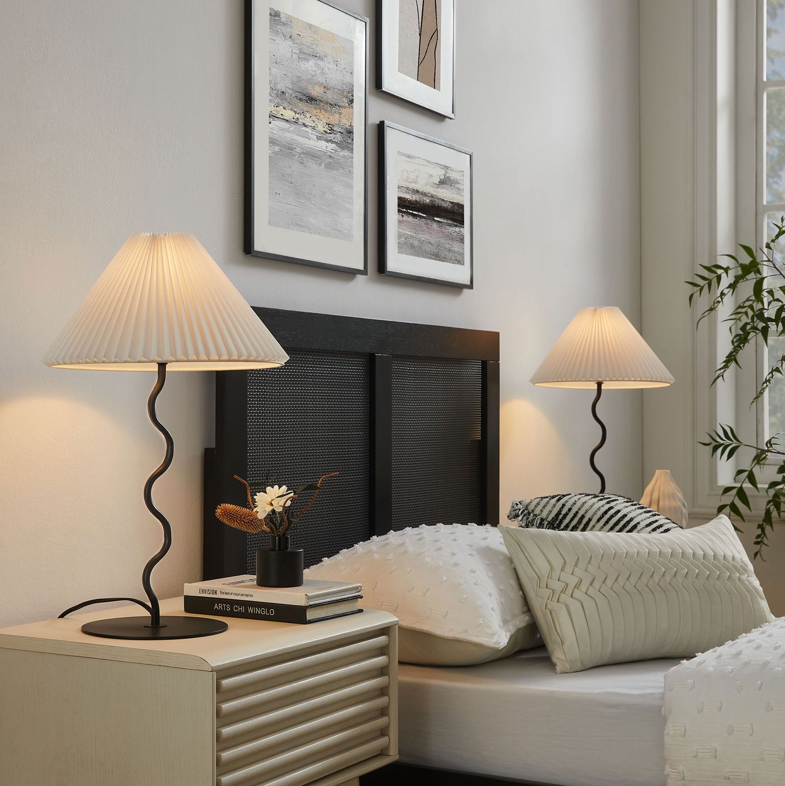 Warmly lit Wave squiggle table lamps casting soft ambient light on each side of a cozy modern bed || EEI-6876-BLK || front_angle_on_room