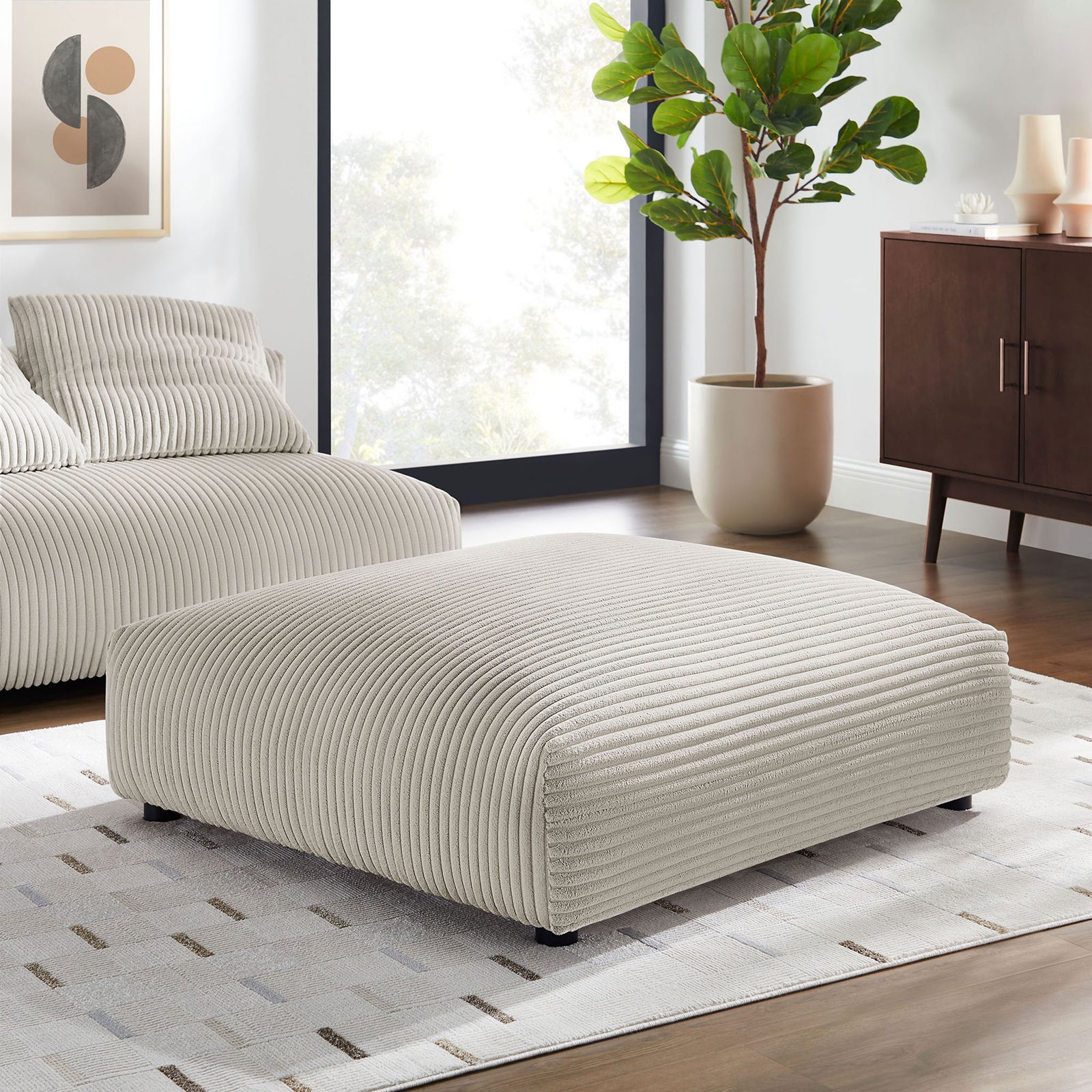 Almond corduroy ottoman anchors a modern living room with coordinating modular seating and decor || EEI-6888-ALM || front_angle_room