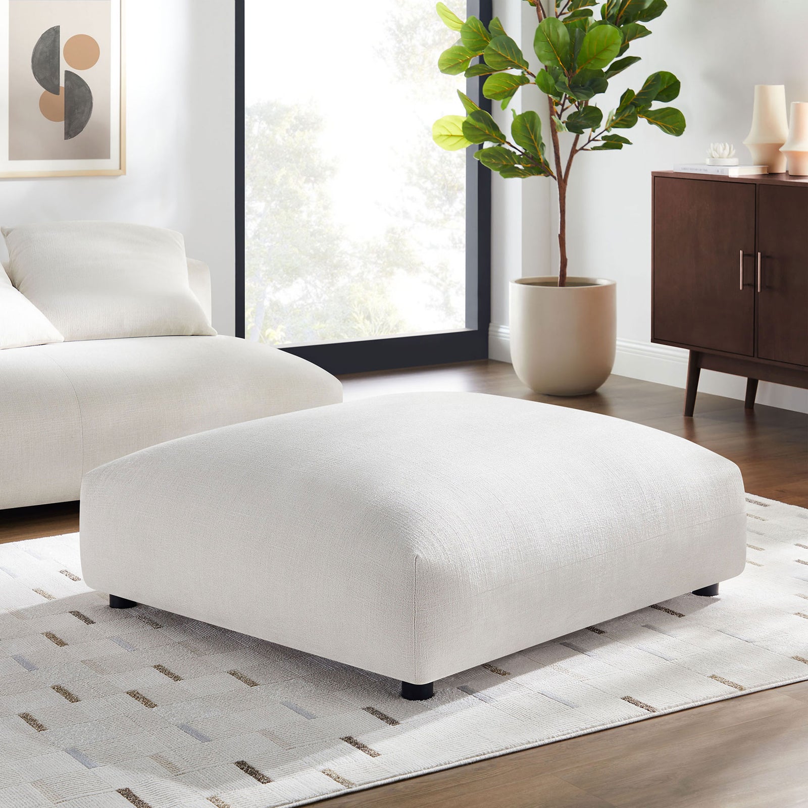 Large salt fabric ottoman acting as a central coffee table in a bright modern living room setup || EEI-6889-SAL || front_angle_room