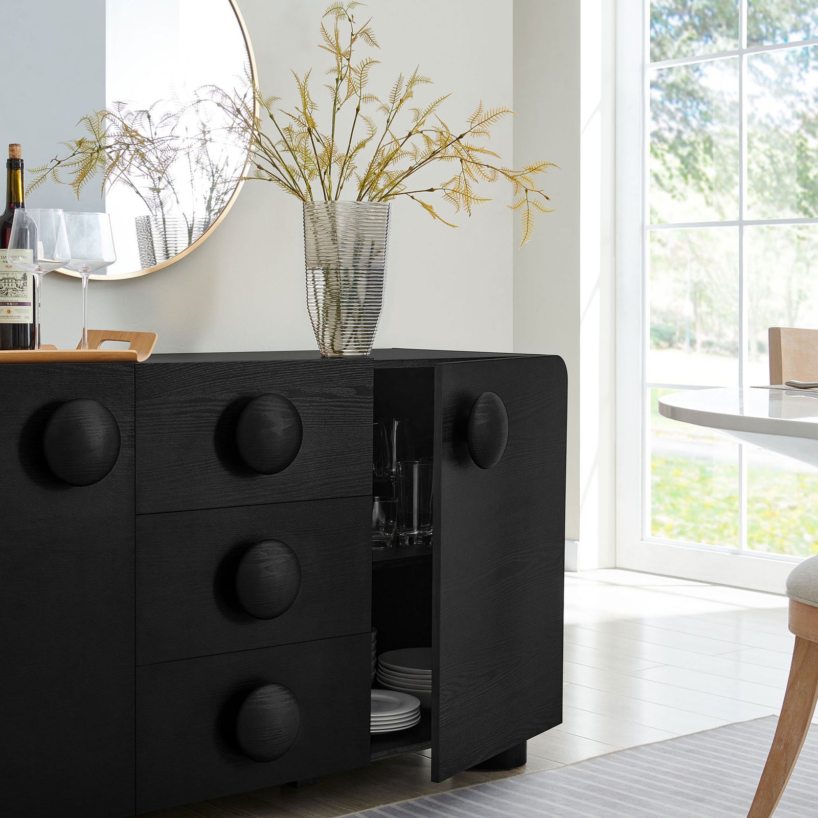 Black Sonnet sideboard styled in a bright dining space, with one door open to display neatly organized serveware || EEI-6892-BLK || front_angle_open_room