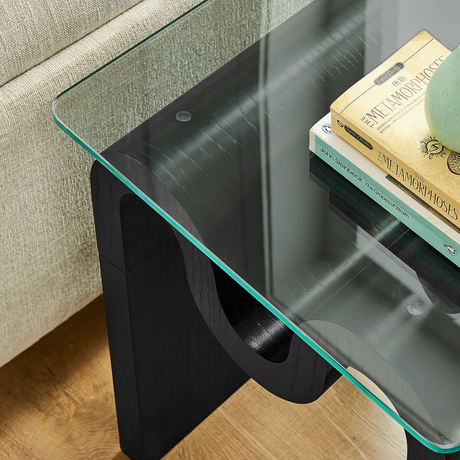 Ondine glass side table styled with books and decor, adding airy modern flair beside a neutral sofa || EEI-6902-BLK || detail_room