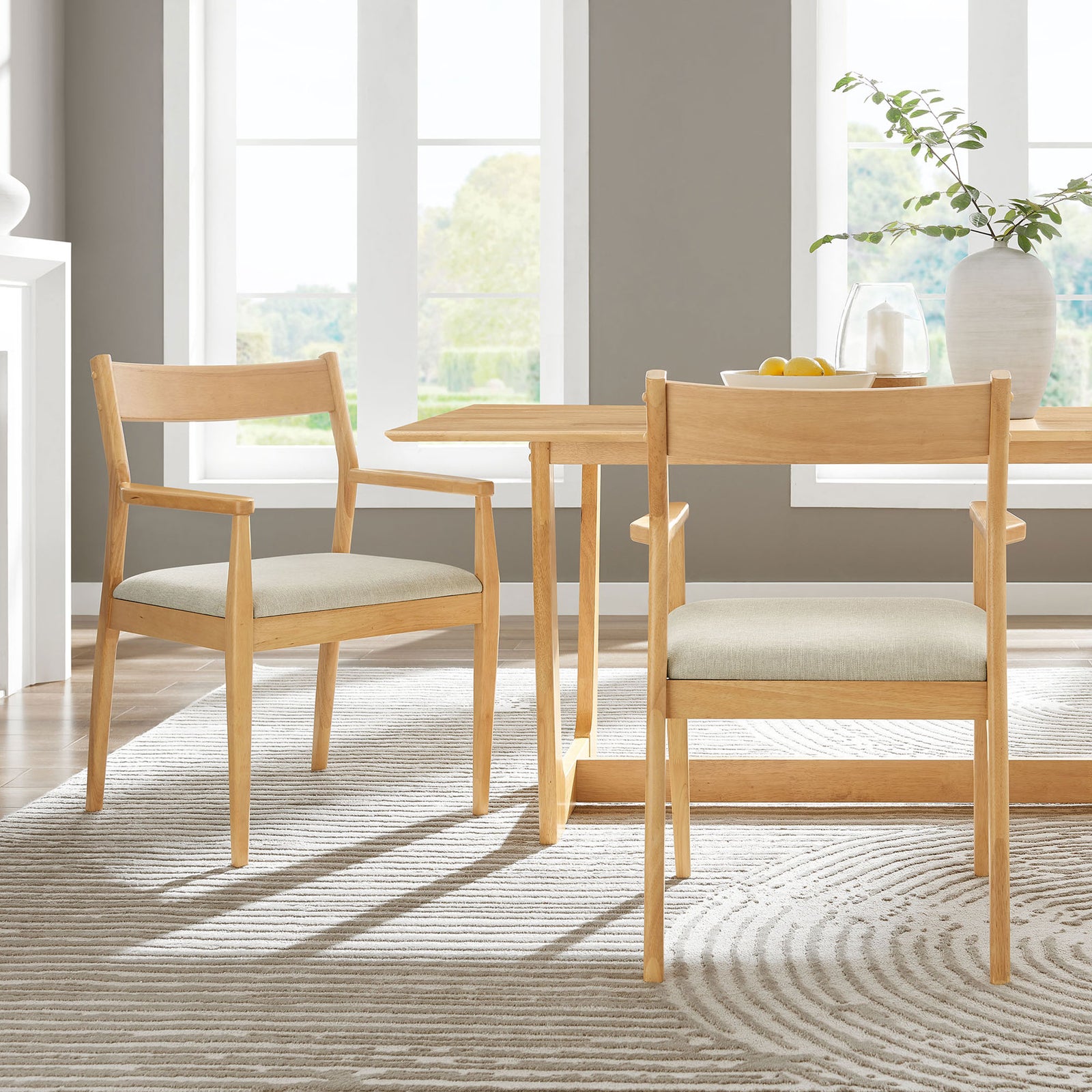 Set of two Solara dining armchairs around a minimalist wood table in a bright, airy dining space. || EEI-6916-NAT-HEB || back_angle_multi_room