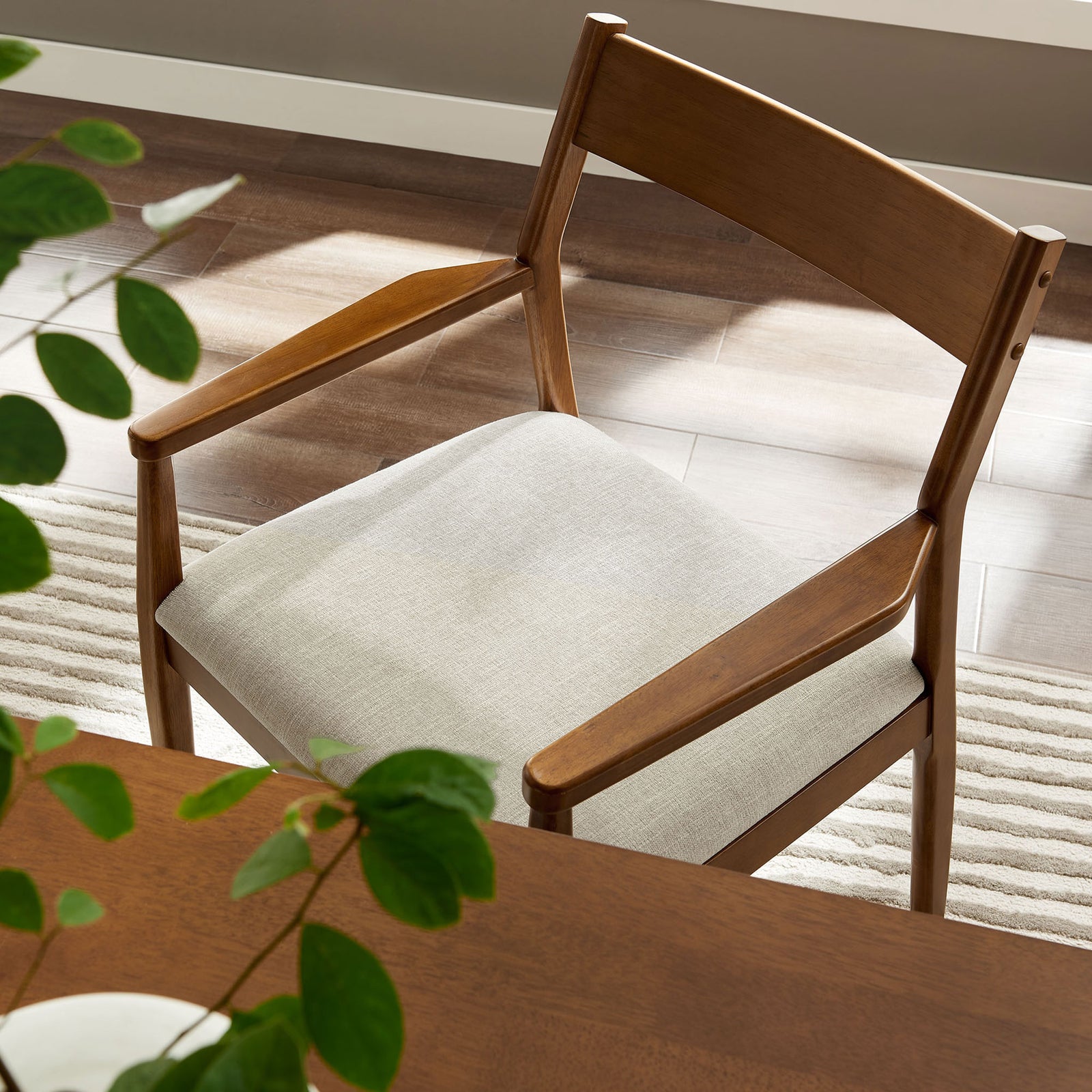 Walnut dining armchair with beige upholstered seat styled beside a wooden dining table and fresh greenery || EEI-6916-WAL-HEB || detail_room