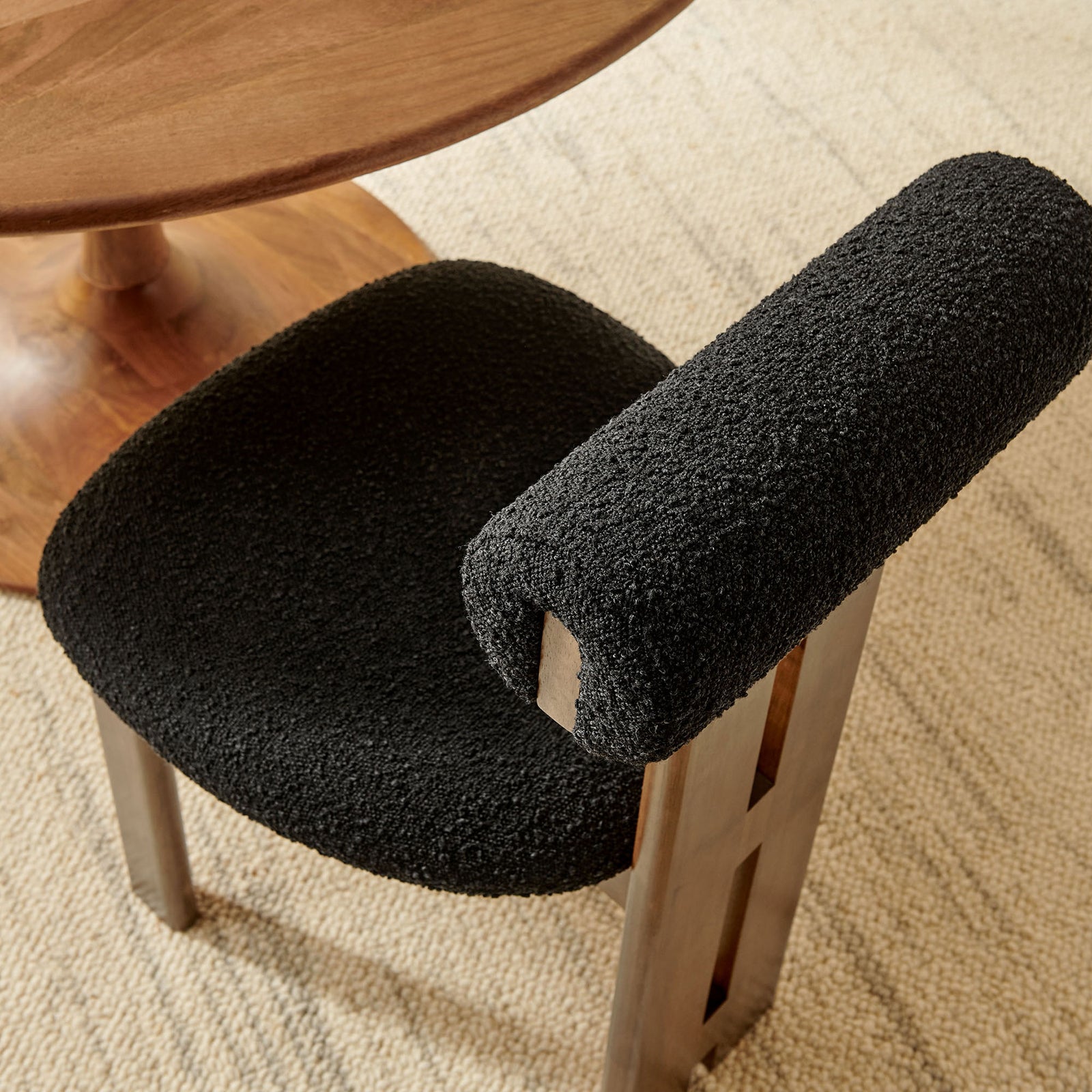 Black boucle dining chair next to a round wood table on a neutral woven rug || EEI-6960-WAL-BLK || top_angle_room