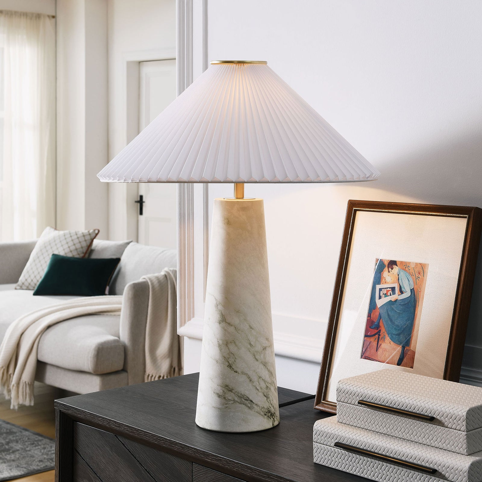 White marble Nera table lamp glowing beside decor on a console in a cozy living room. || EEI-6963-WHI || front_on_room