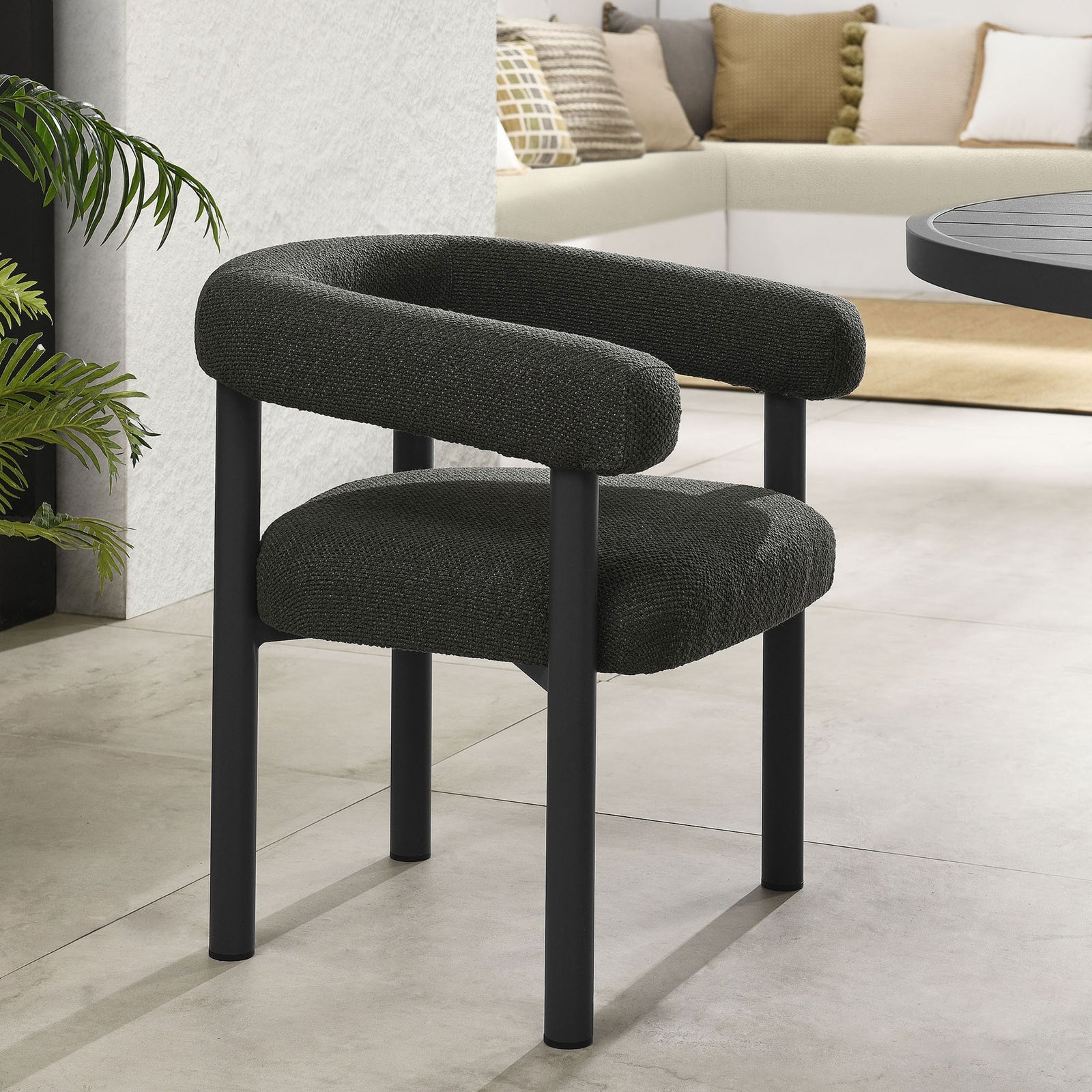 Charcoal graphite upholstered patio dining chair beside a modern outdoor table with lush greenery accents || EEI-6979-CHA-GPH || front_angle_room