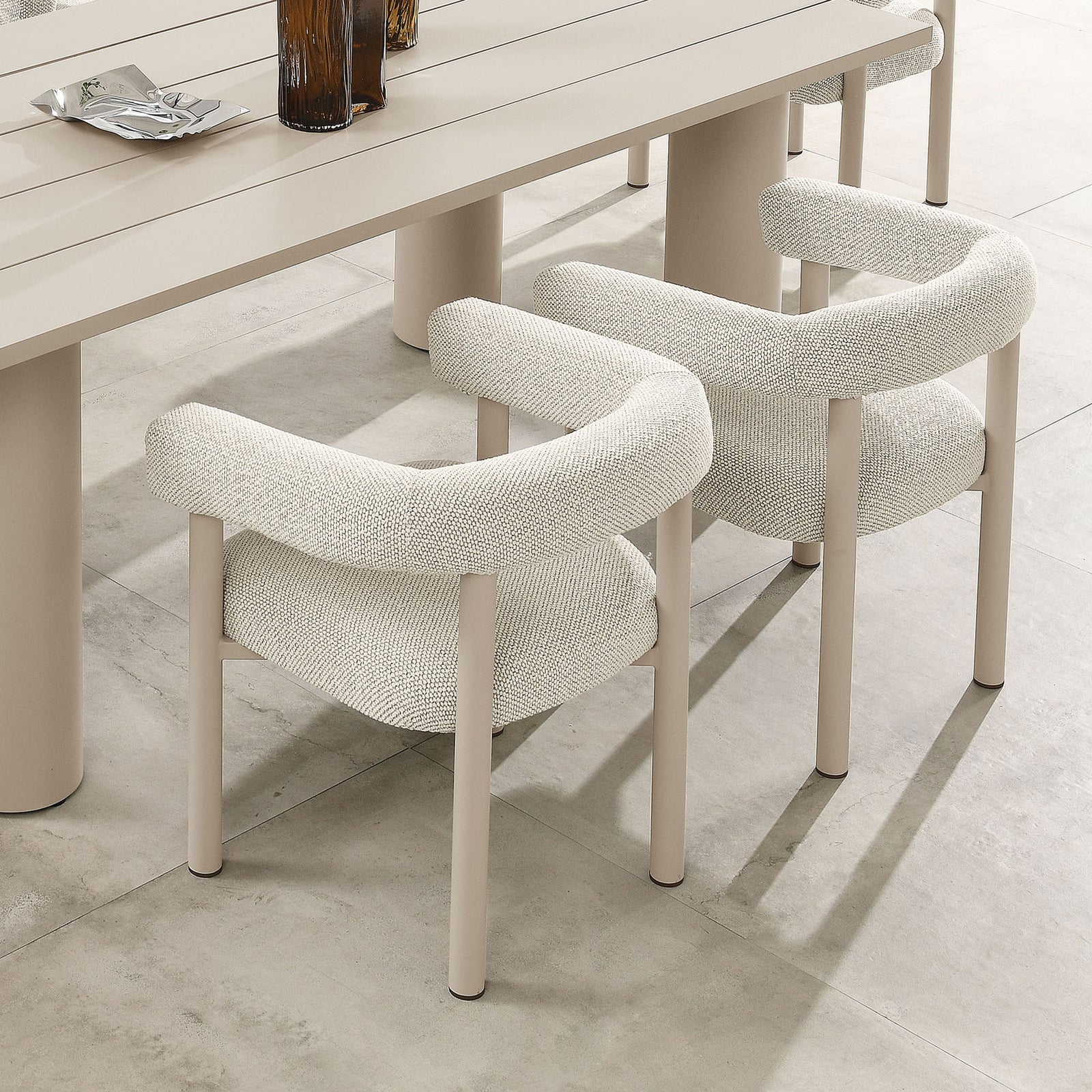 Pair of ivory armchairs surrounding a taupe outdoor dining table on a spacious stone patio || EEI-6979-IVO-TAU || front_angle_multi_room