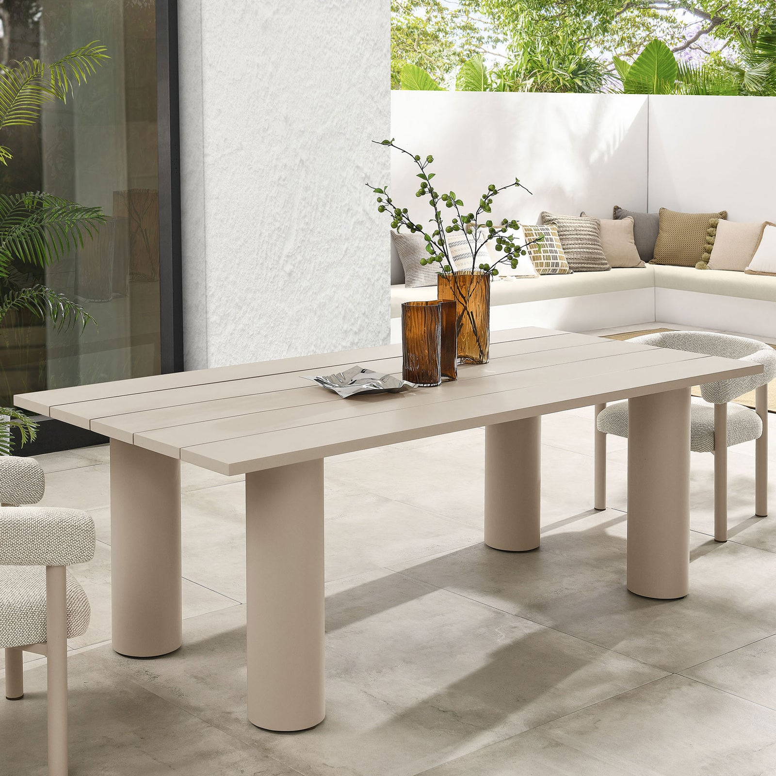 Taupe aluminum patio dining table styled with textured chairs and amber glass vases on a bright modern terrace || EEI-6980-TAU || front_angle_room