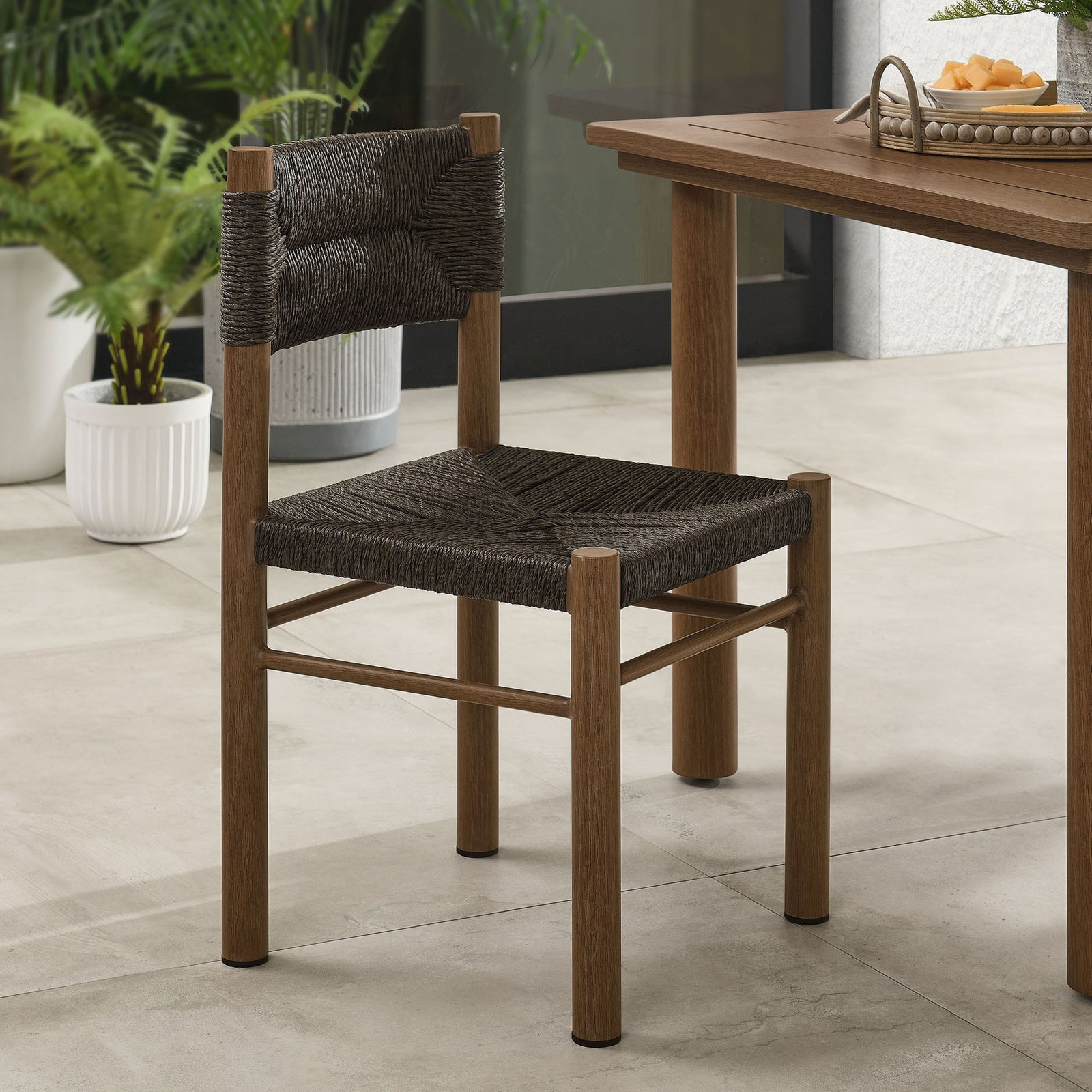 Walnut rattan dining chair styled at an outdoor table with greenery, creating a cozy modern patio scene || EEI-6982-WAL || front_angle_room