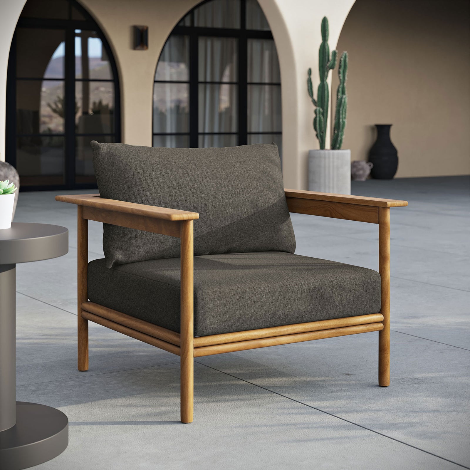 Charcoal cushioned teak patio armchair styled on a spacious terrace with arched outdoor architecture || EEI-7007-NAT-FLI || front_angle_room