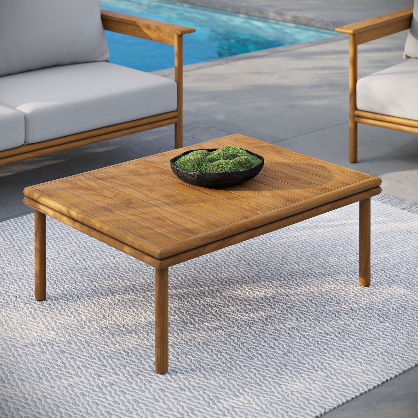 Teak outdoor coffee table on patio rug paired with cushioned seating beside a swimming pool || EEI-7010-NAT || front_angle_room