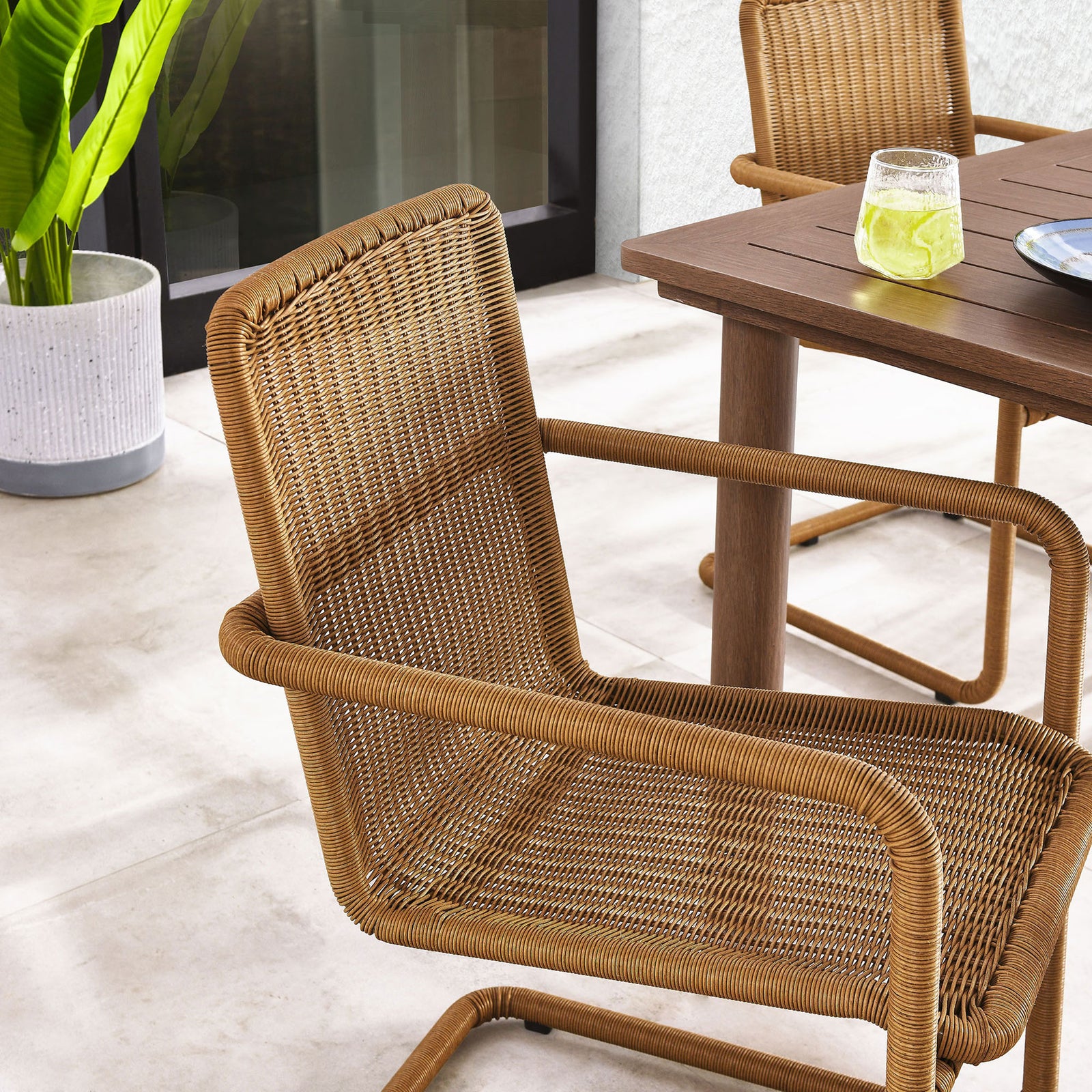 Natural wicker patio chair pulled up to a dining table adding warm texture to a modern outdoor space || EEI-7014-NAT || detail_room