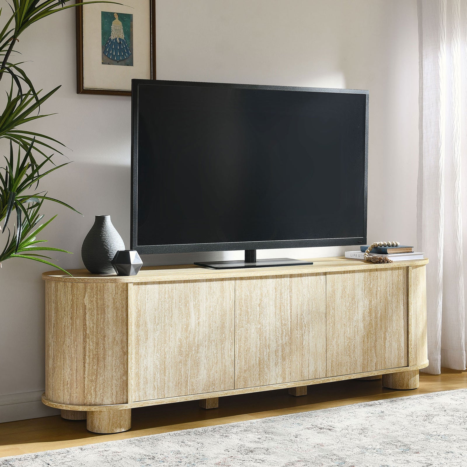 Overture faux travertine TV stand styled in a bright living room supporting a large flat-screen TV || EEI-7016-TRA || front_angle_room