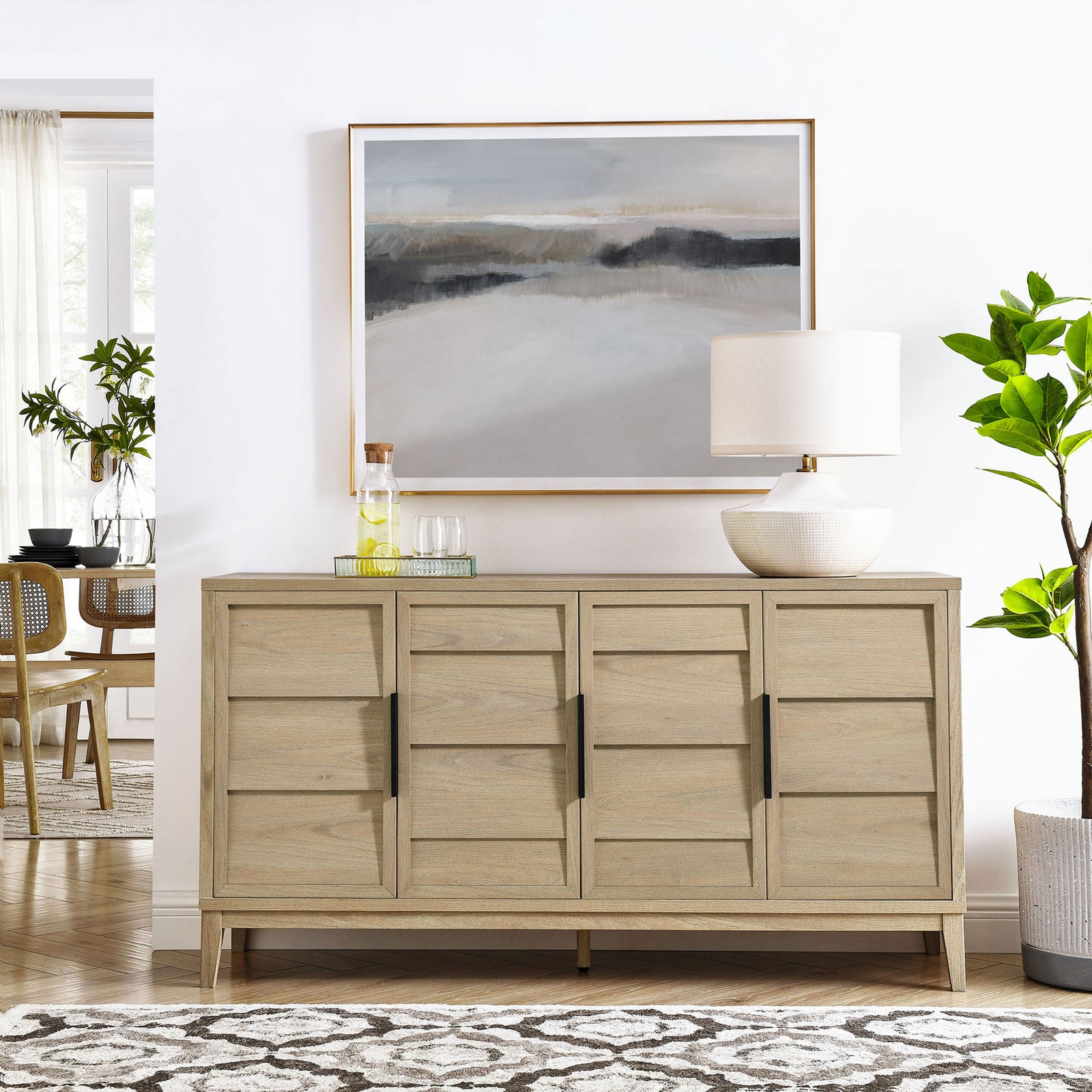 Sinya light oak sideboard styled in a bright dining space with artwork, lamp, and greenery. || EEI-7040-LOA || front_room