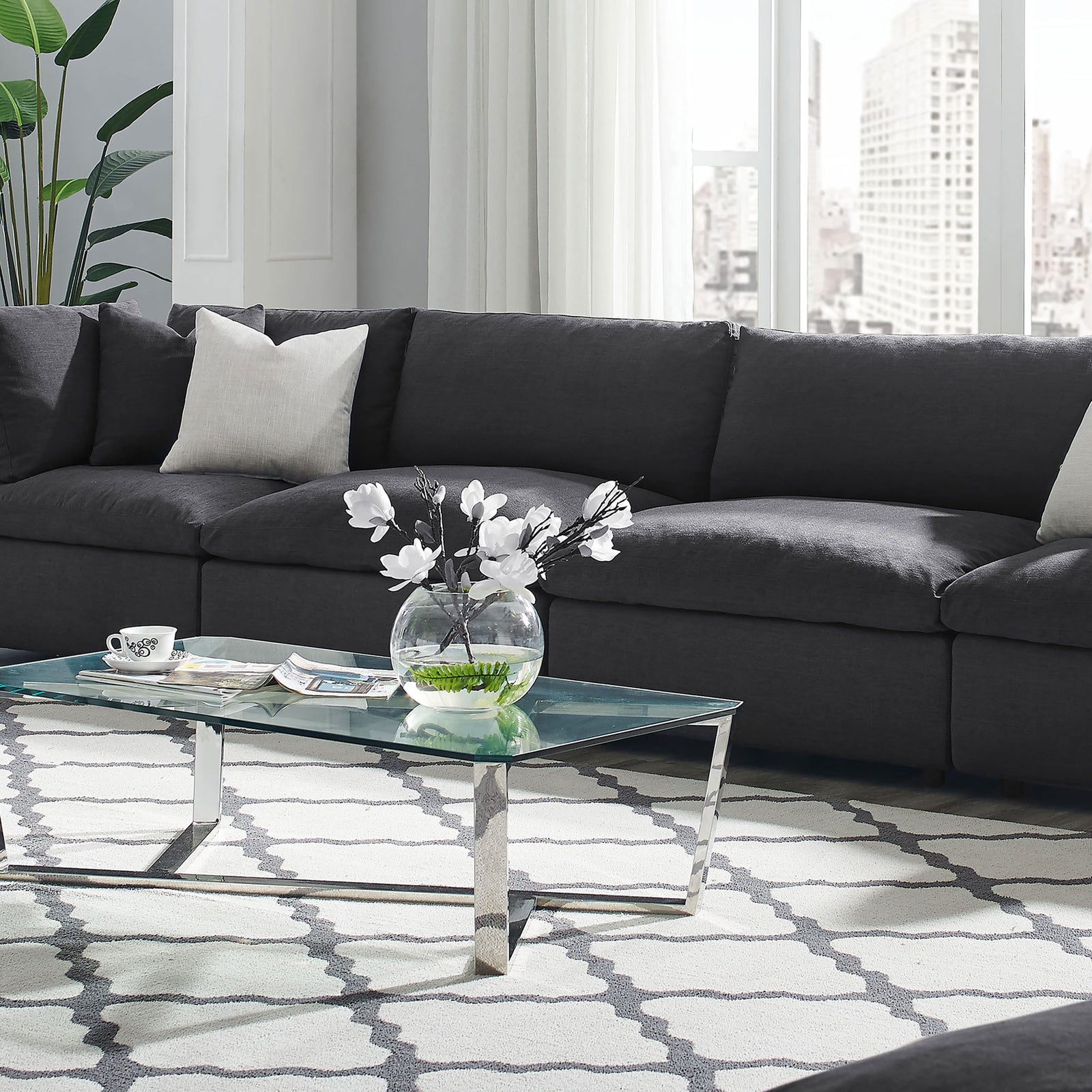 Gray overstuffed sectional sofa styled in a bright modern living room with glass coffee table and patterned area rug || EEI-7043-GRY || front_angle_room