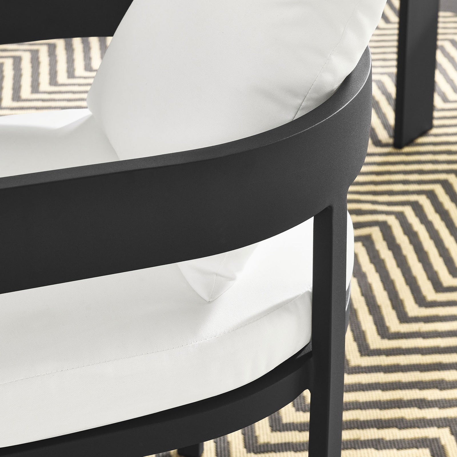 Detail of charcoal patio dining chair arm and white cushions over a geometric outdoor rug by the table || EEI-7053-GRY-WHI || detail_room