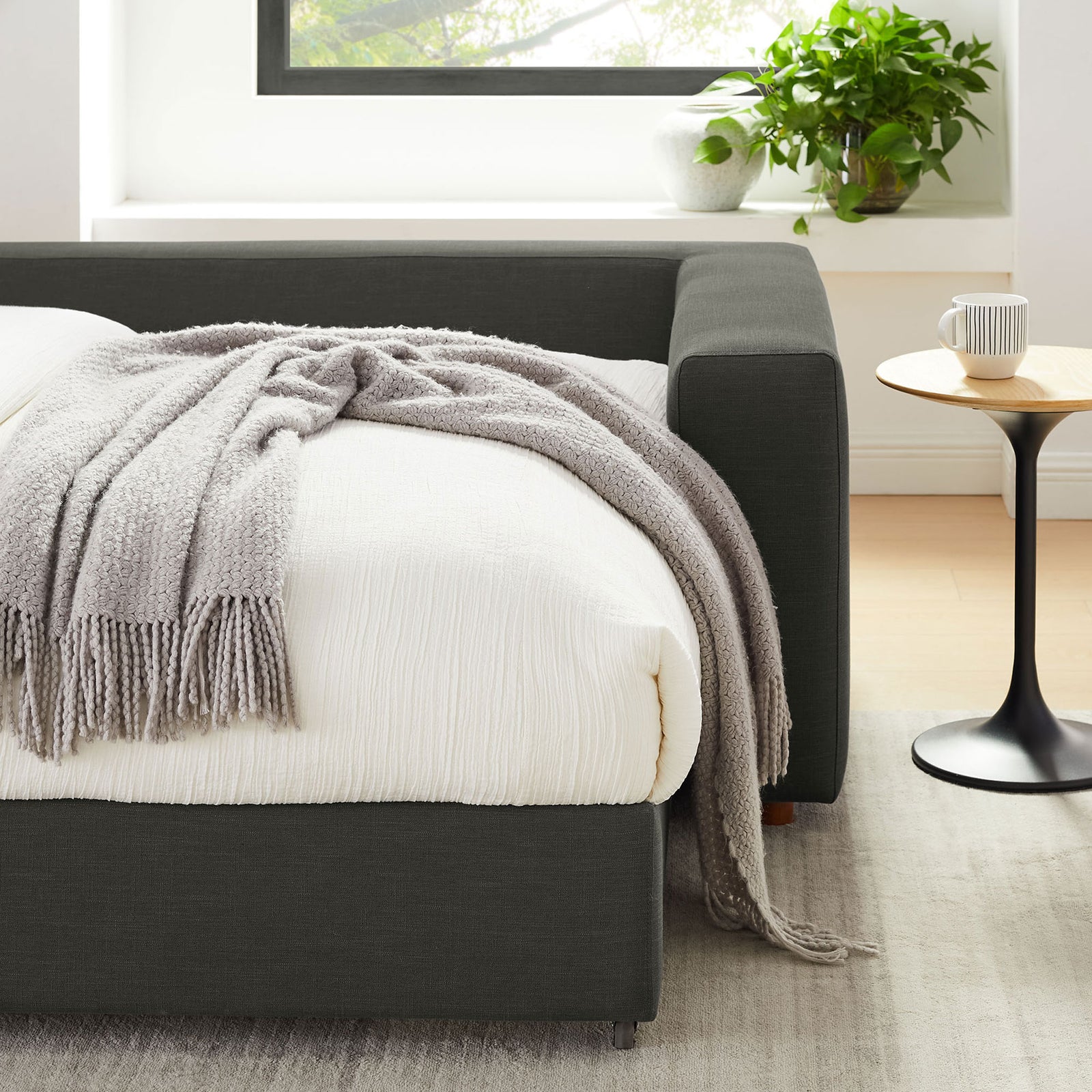 Cozy corner of gray sleeper sofa bed styled with soft blanket, accent table, and greenery || EEI-7080-GRY || detail_room