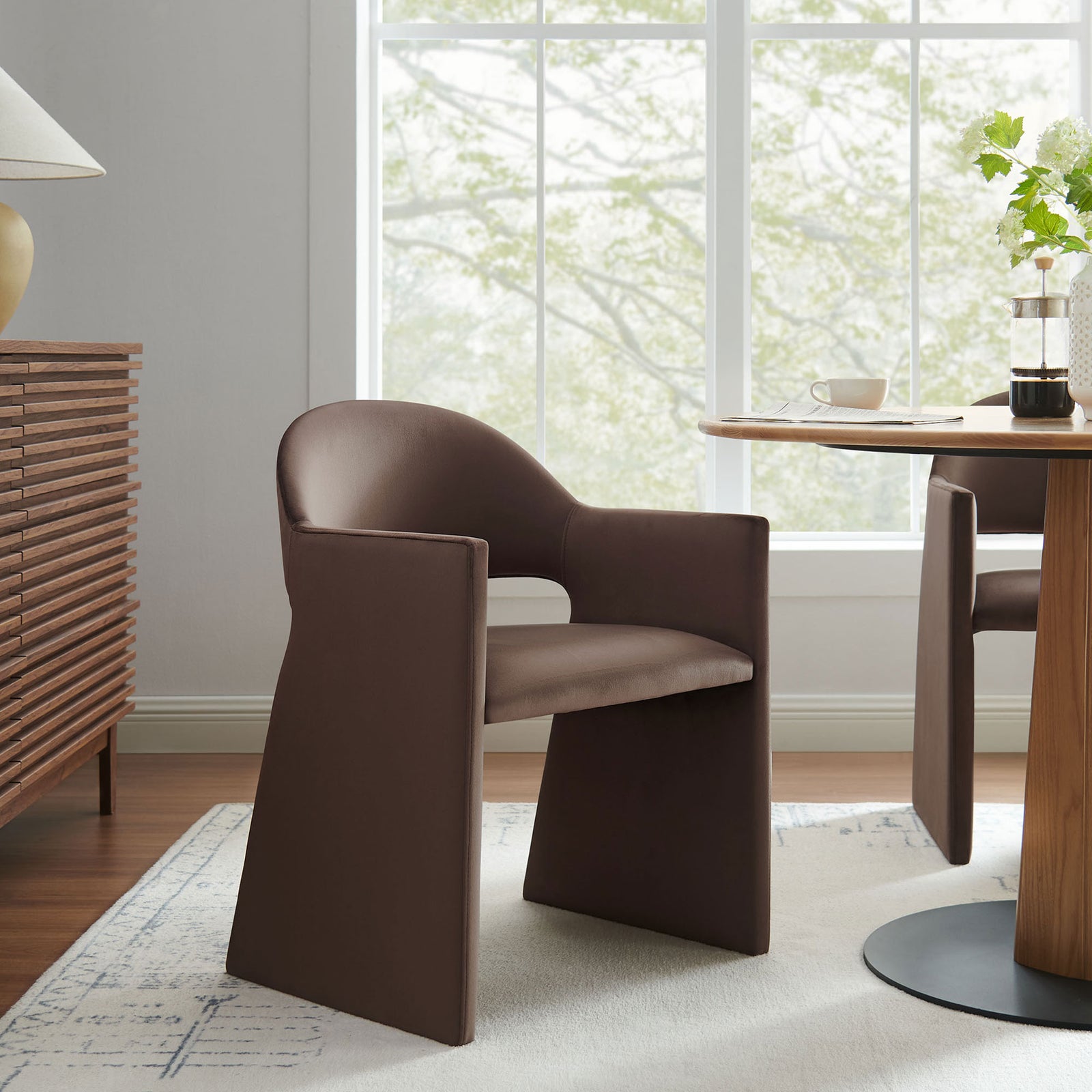 Talia chocolate velvet dining armchair styled at a round dining table, adding sculptural comfort to a modern room. || EEI-7081-CHB || front_angle_room