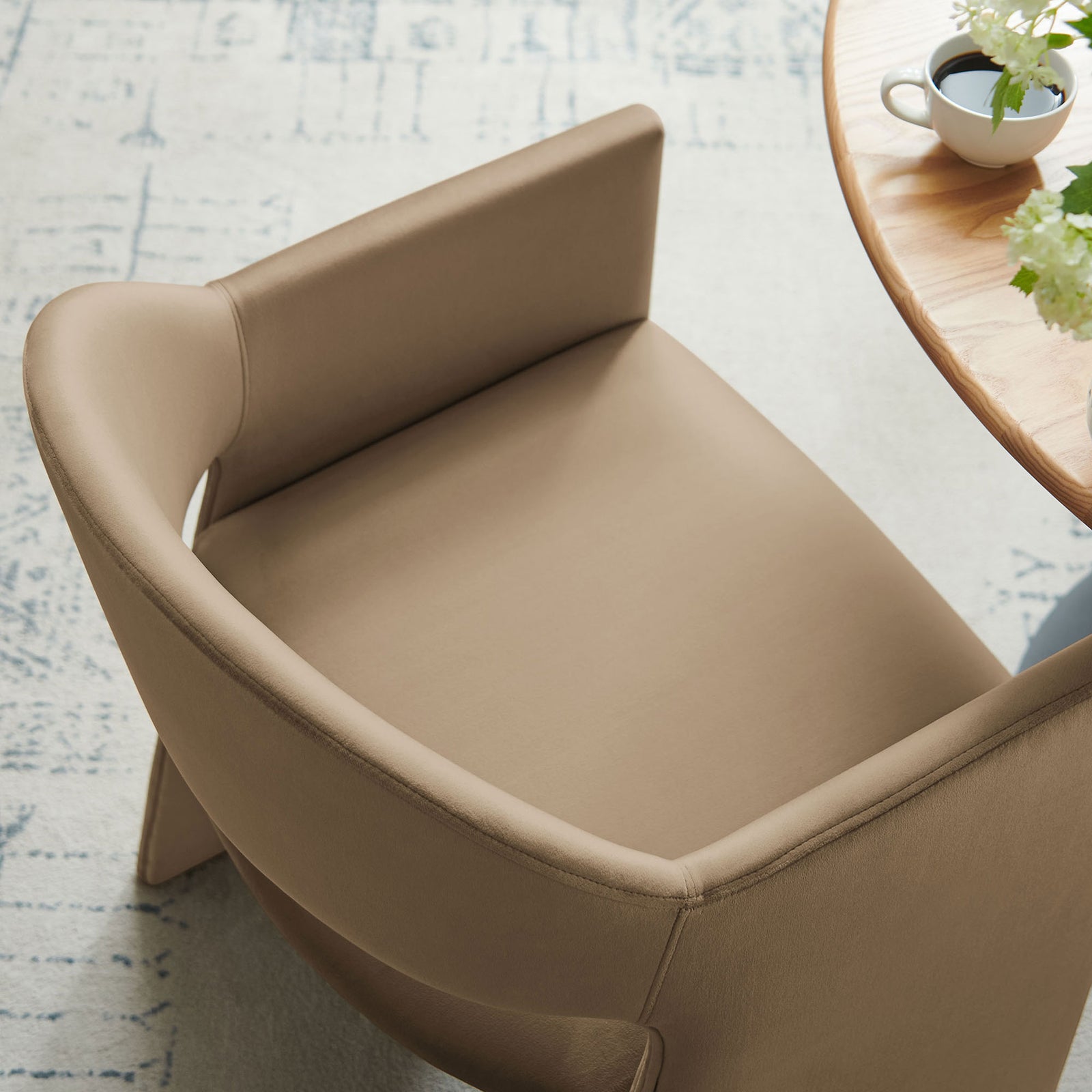 Taupe velvet dining armchair tucked at a round wood table, showing the curved back and roomy seat || EEI-7081-TAU || top_angle_room