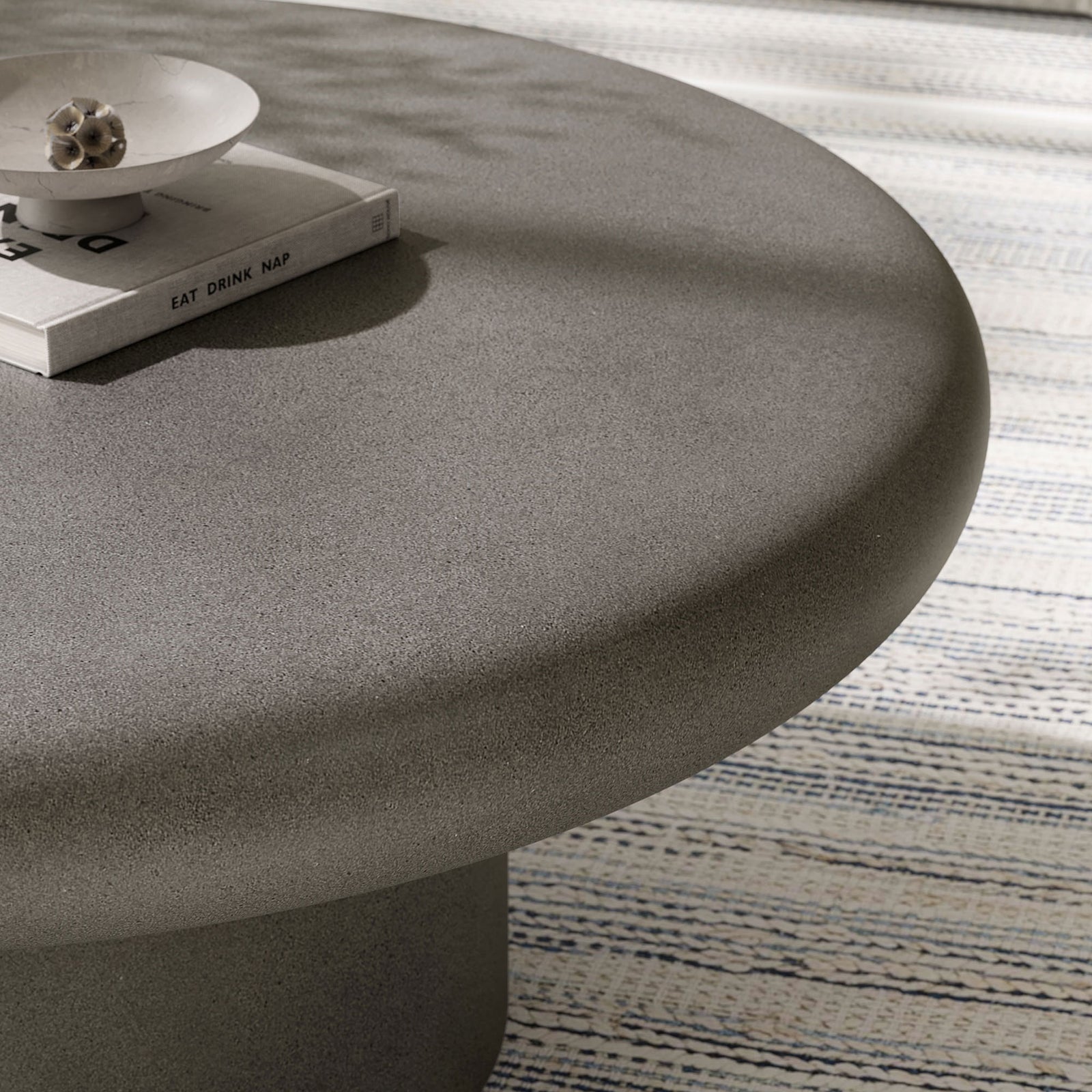 Gray concrete coffee table surface styled with decor, adding soft texture and modern contrast atop a woven rug || EEI-7092-GRY || detail_room
