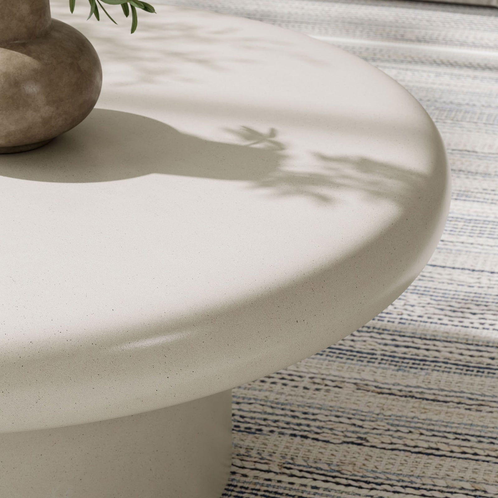 White concrete coffee table surface styled with decor, adding airy texture and softness atop a woven rug || EEI-7092-WHI || detail_room