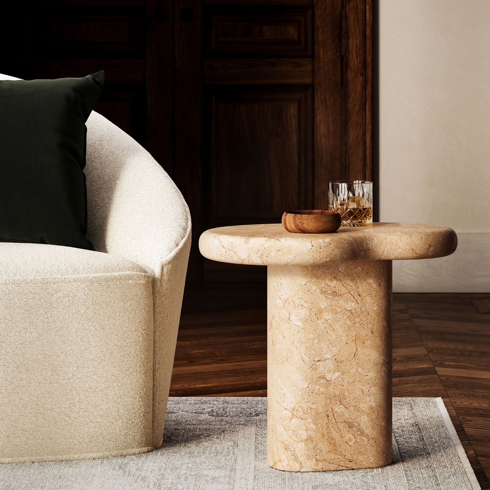 Faux travertine pedestal side table in a cozy living room next to a plush chair and soft area rug || EEI-7094-TRV || front_angle_room