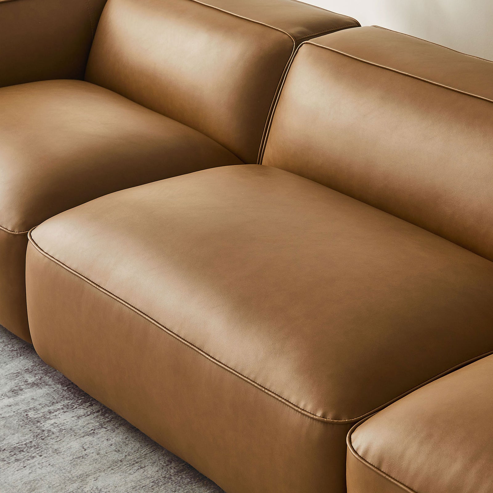 Softly rounded cushions and tailored stitching on the camel Auren modular sofa in a modern living room || EEI-7132-CAM || detail_room