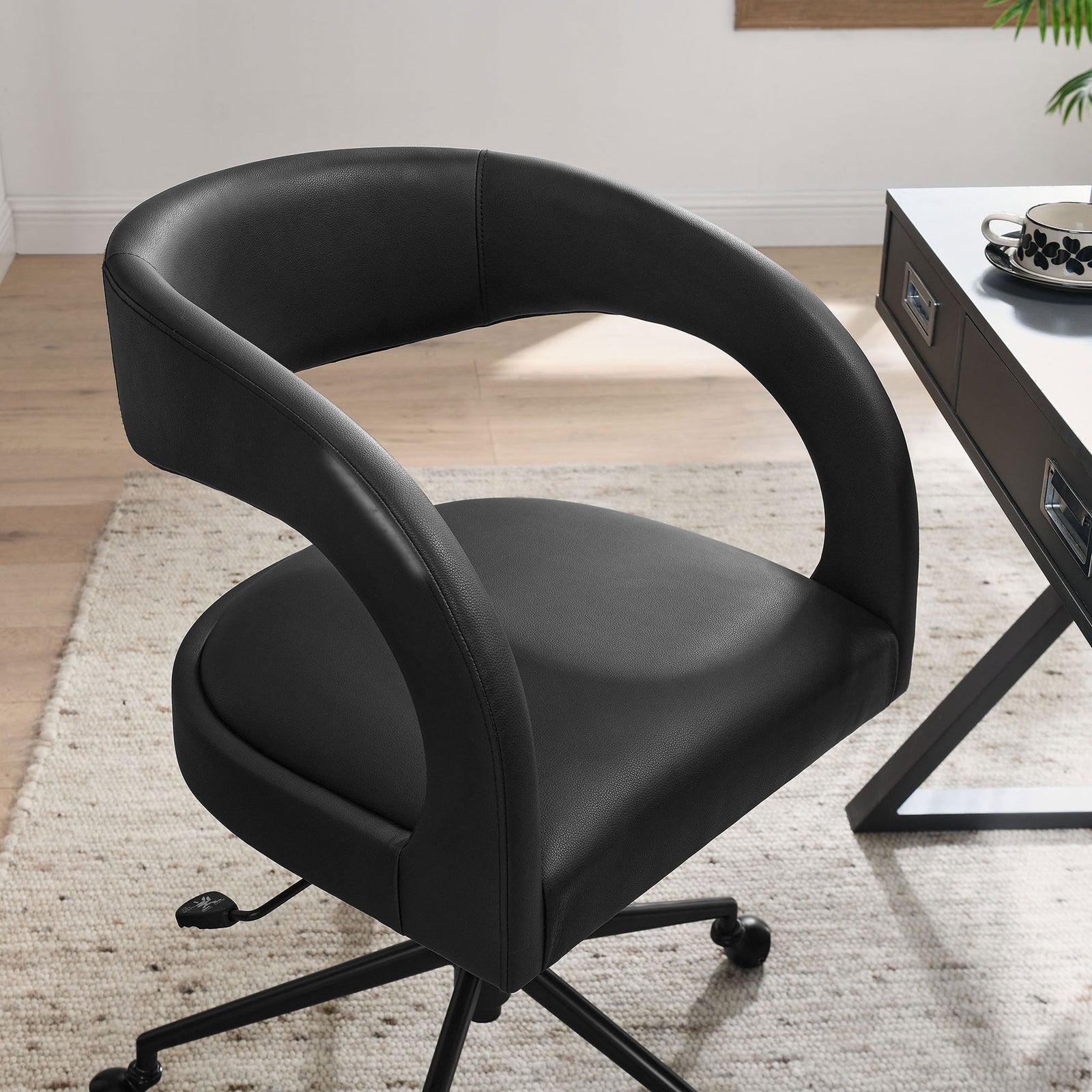 Black vegan leather office chair styled next to a modern desk on a neutral area rug. || EEI-7150-BLK || front_angle_room