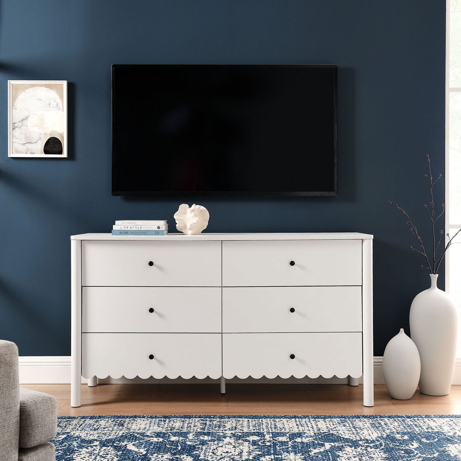 White scalloped dresser anchors this living space beneath a large TV, pairing storage with modern charm || EEI-7157-WHI || front_room