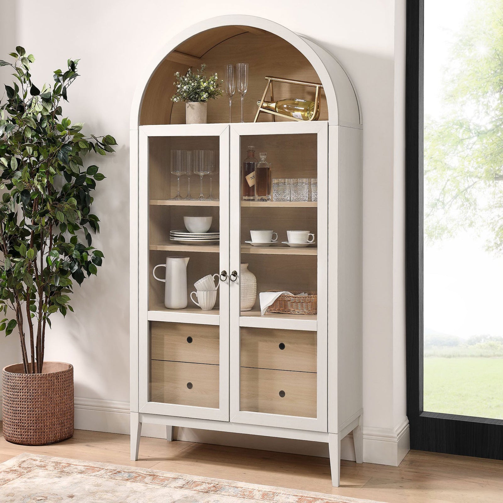 Ivory oak display cabinet arranged as a bar with glassware and bottles beside a tall window || EEI-7168-IVO-OAK || front_angle_room