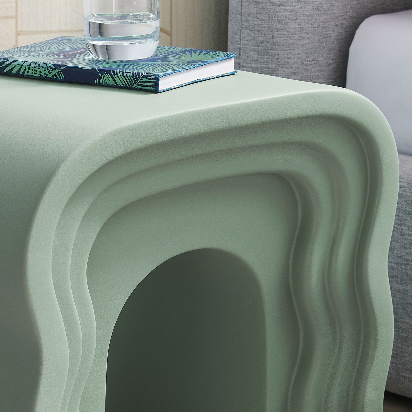 Sage squiggle side table styled beside a sofa with a book and glass for playful retro charm || EEI-7171-SGE || detail_room