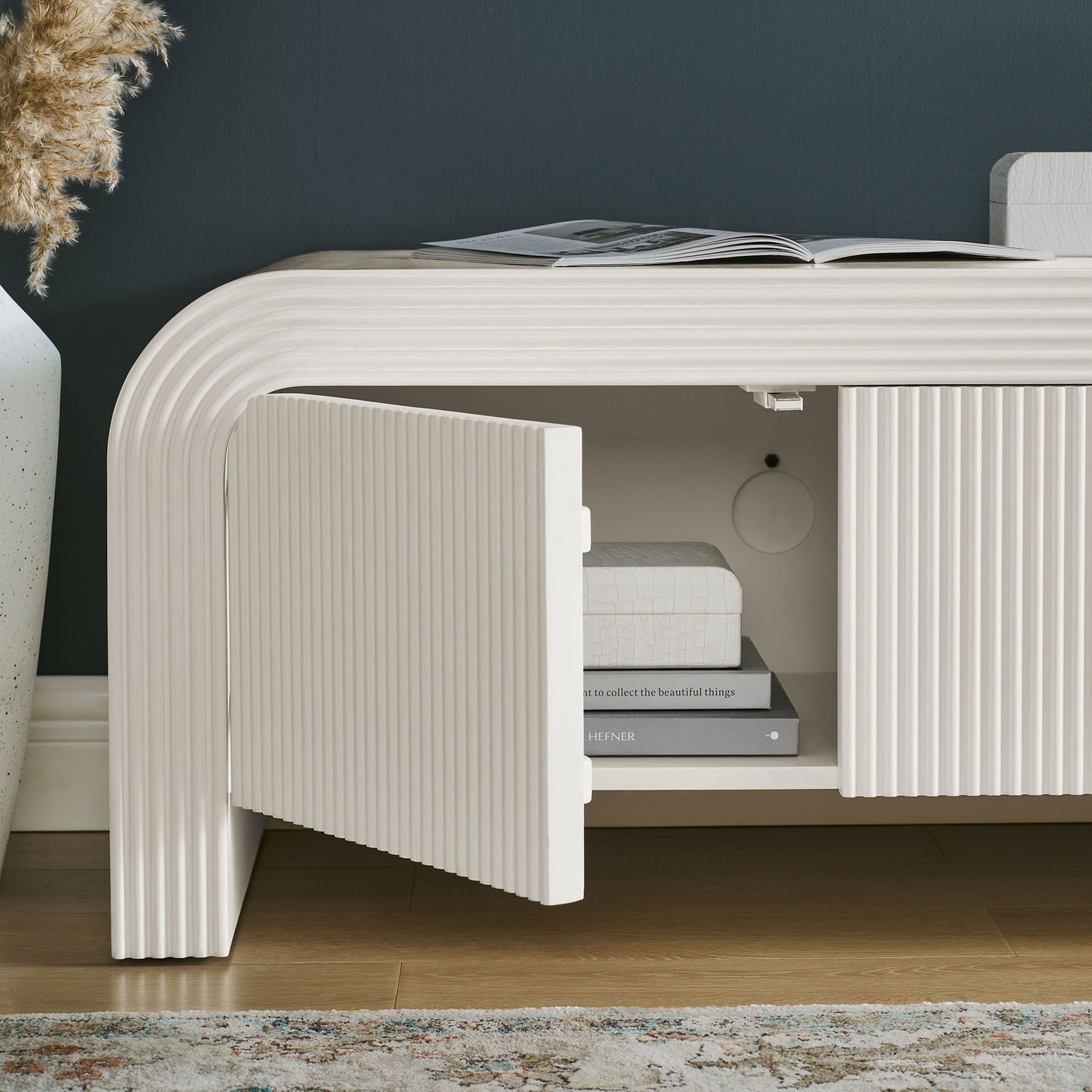 Styled white matte TV stand cabinet with one door open to display interior shelving and books || EEI-7199-IVO || storage_open_room