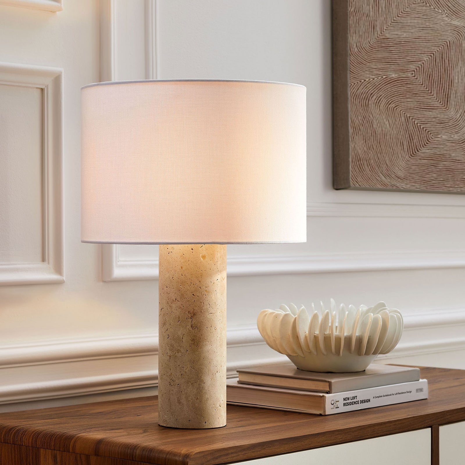 Zenith travertine table lamp casting soft glow over console table and sculptural decor || EEI-7213-TRV || front_angle_on_room