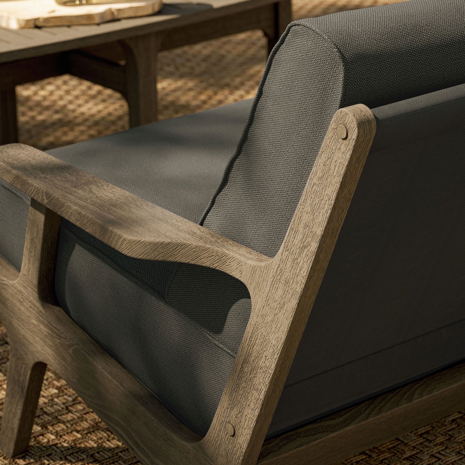 Saratoga loveseat on woven outdoor rug showing the sculpted teak frame and dark flint gray cushions. || EEI-7247-WGR-FLI || detail_room
