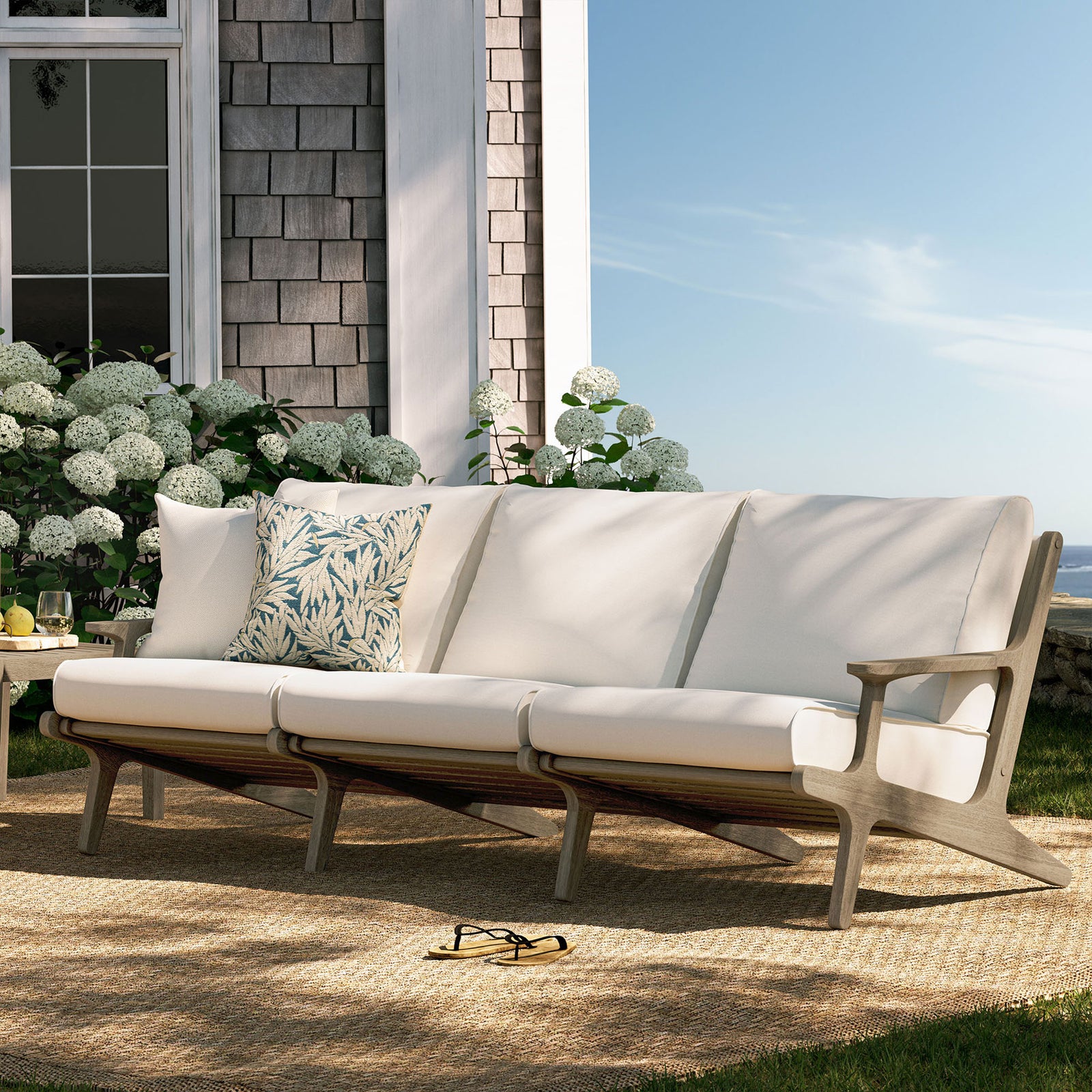 Saratoga teak sofa arranged on a sunny patio with white cushions and patterned accent pillows || EEI-7249-WGR-WHI || front_angle_room