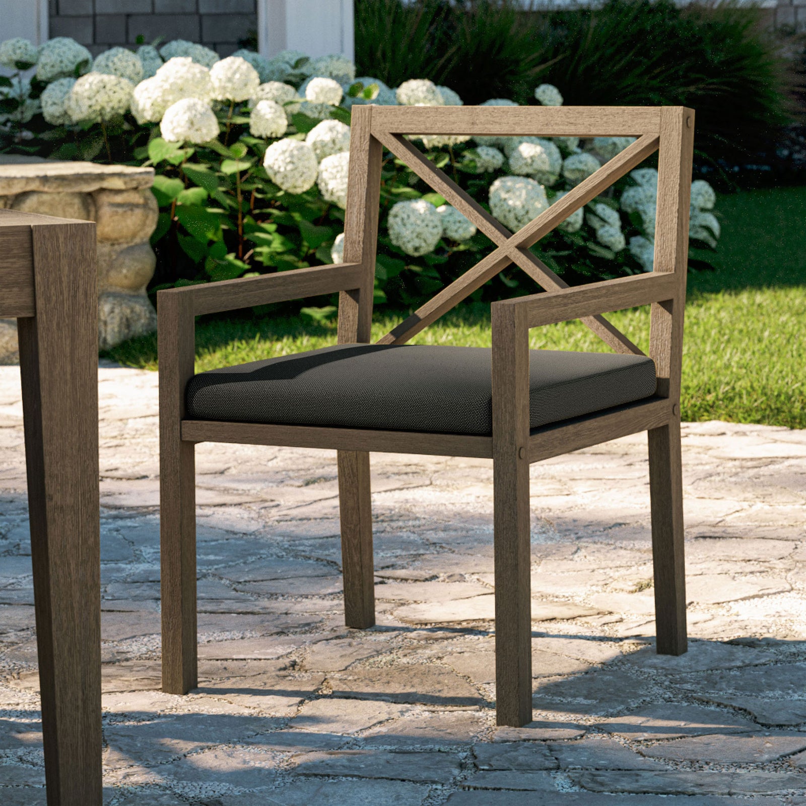 Northlake teak armchair with charcoal cushion styled beside an outdoor dining table on a stone patio. || EEI-7253-WGR-FLI || front_angle_room
