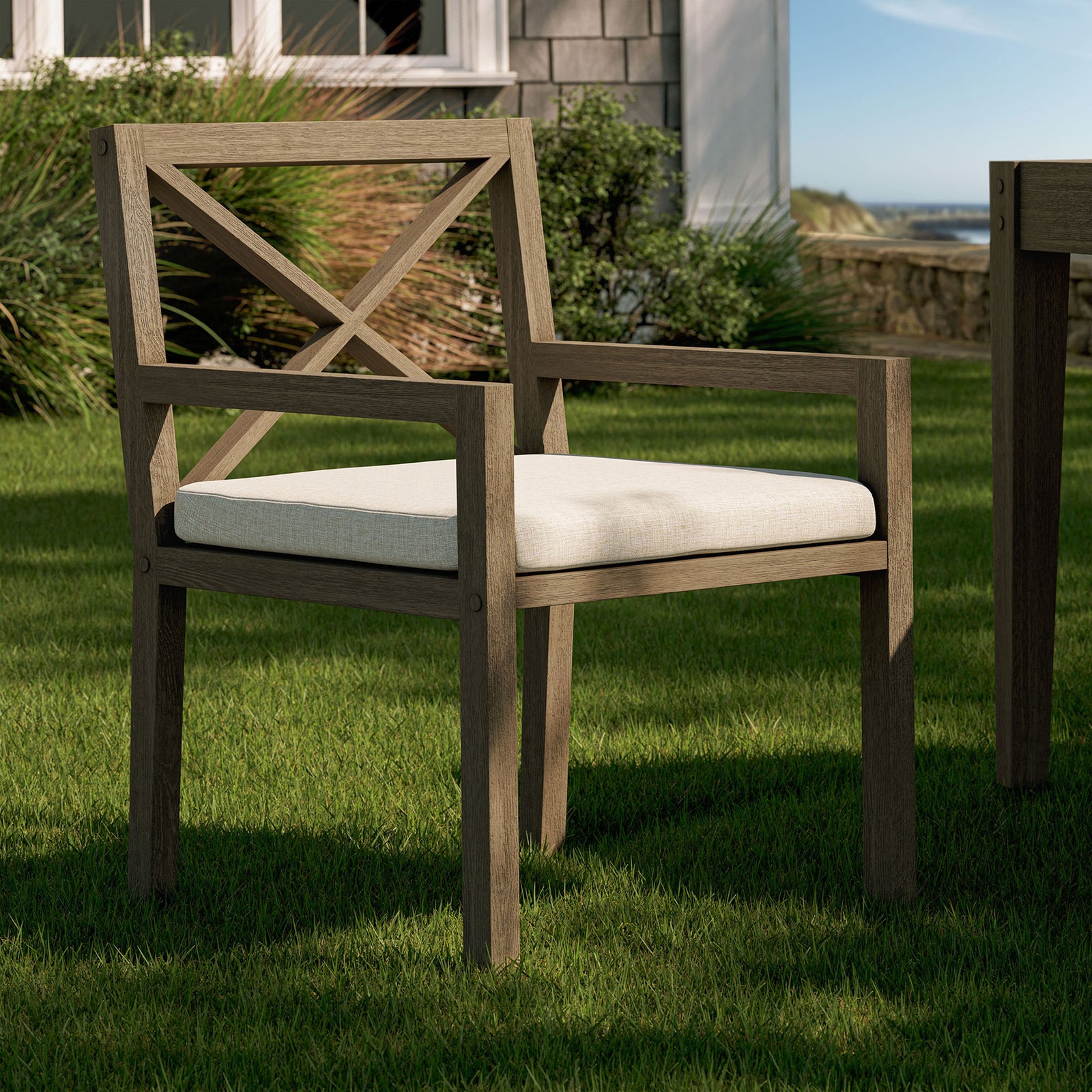 Northlake teak armchair with pebble cushion arranged on a green lawn beside an outdoor dining set. || EEI-7253-WGR-PEB || front_angle_room