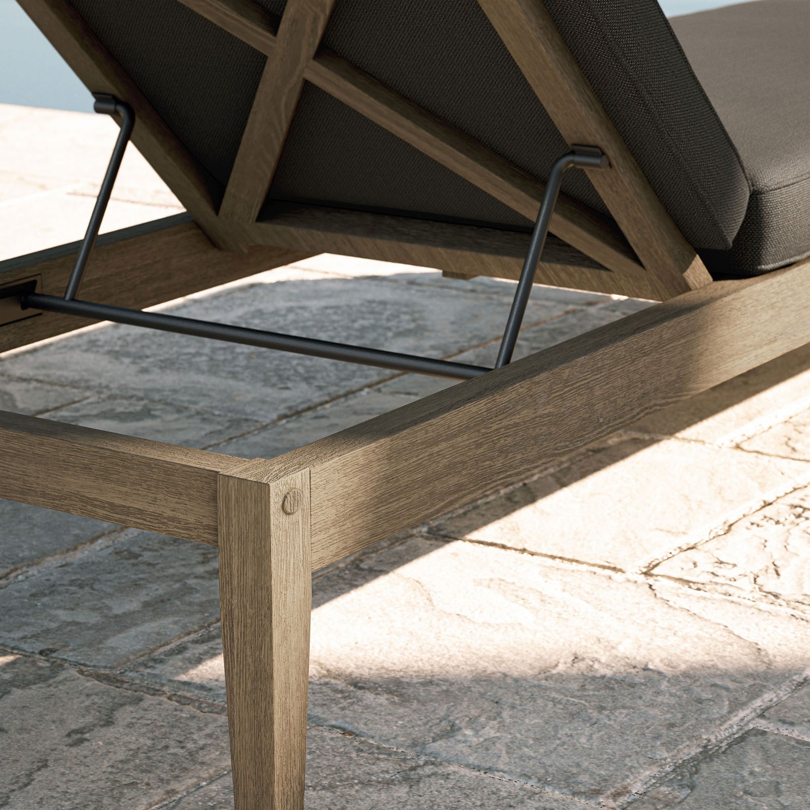 Weathered teak frame and dark gray cushion detail shown beside a sunlit stone poolside patio || EEI-7256-WGR-FLI || detail_room