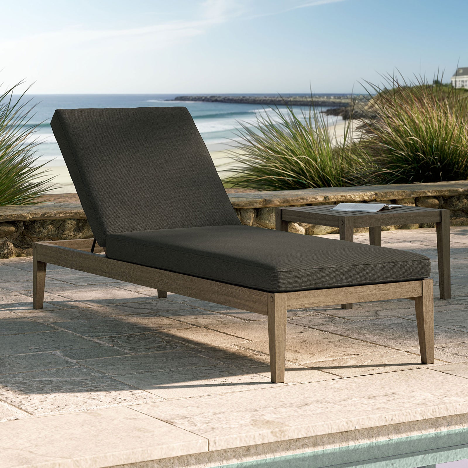 Outdoor teak chaise lounge with dark gray cushion styled by a pool with coastal landscape in the background || EEI-7256-WGR-FLI || front_angle_converted_room