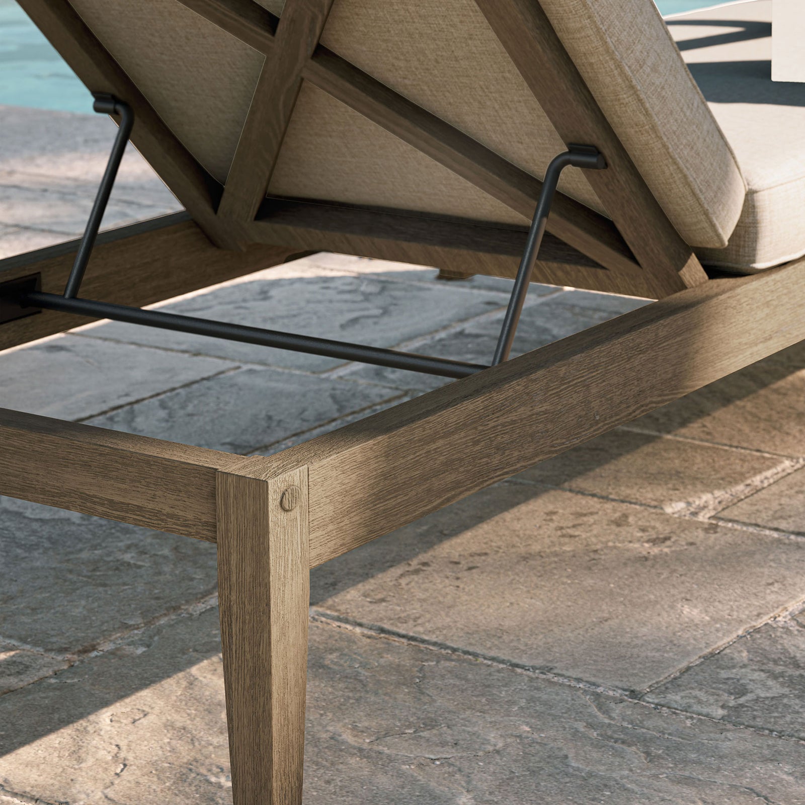Weathered teak frame and light pebble cushion detail shown beside a sunlit stone poolside patio || EEI-7256-WGR-PEB || detail_room