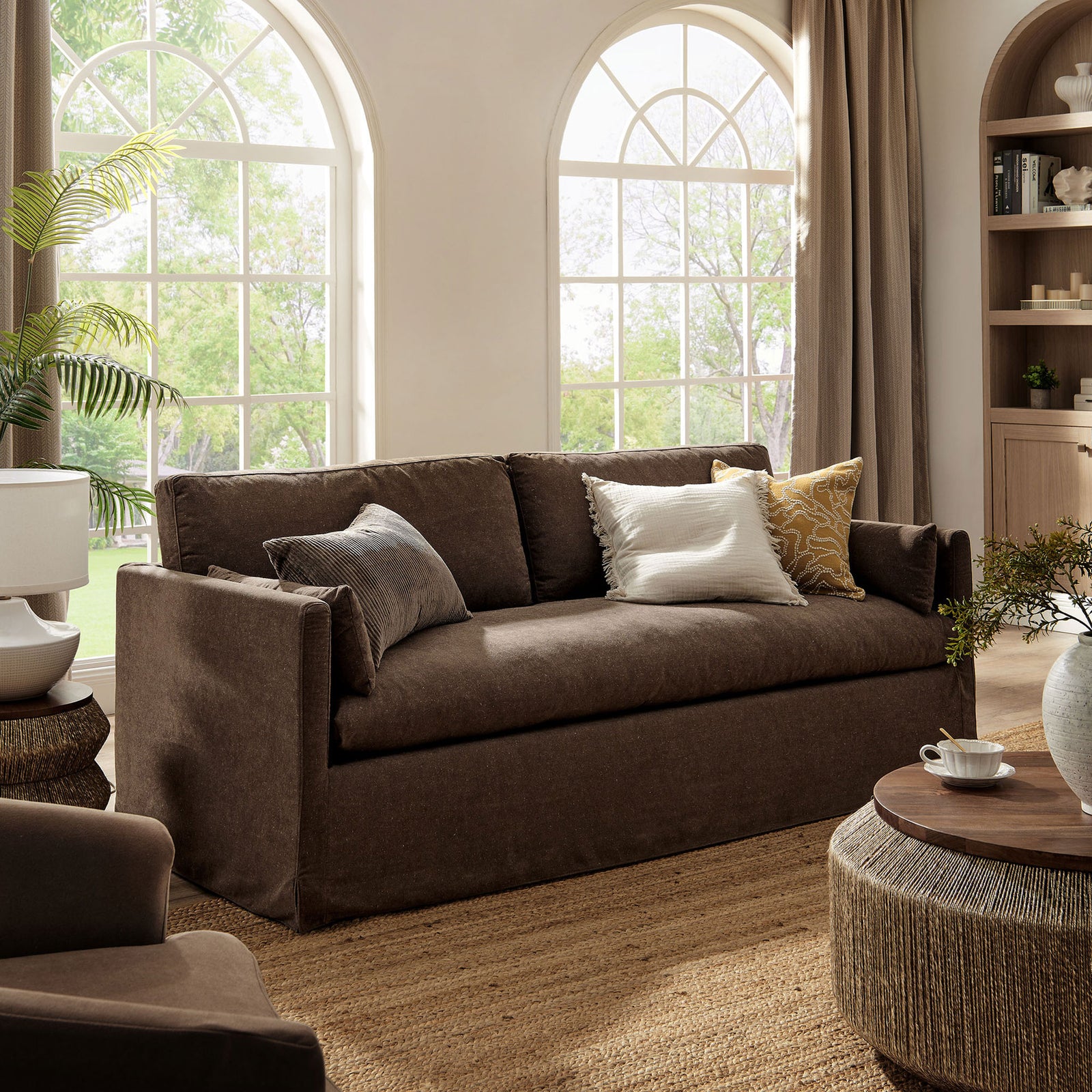 Inviting cocoa slipcovered sofa framed by arched windows, warm drapery, and layered neutral decor accents. || EEI-7260-COA || front_angle_room