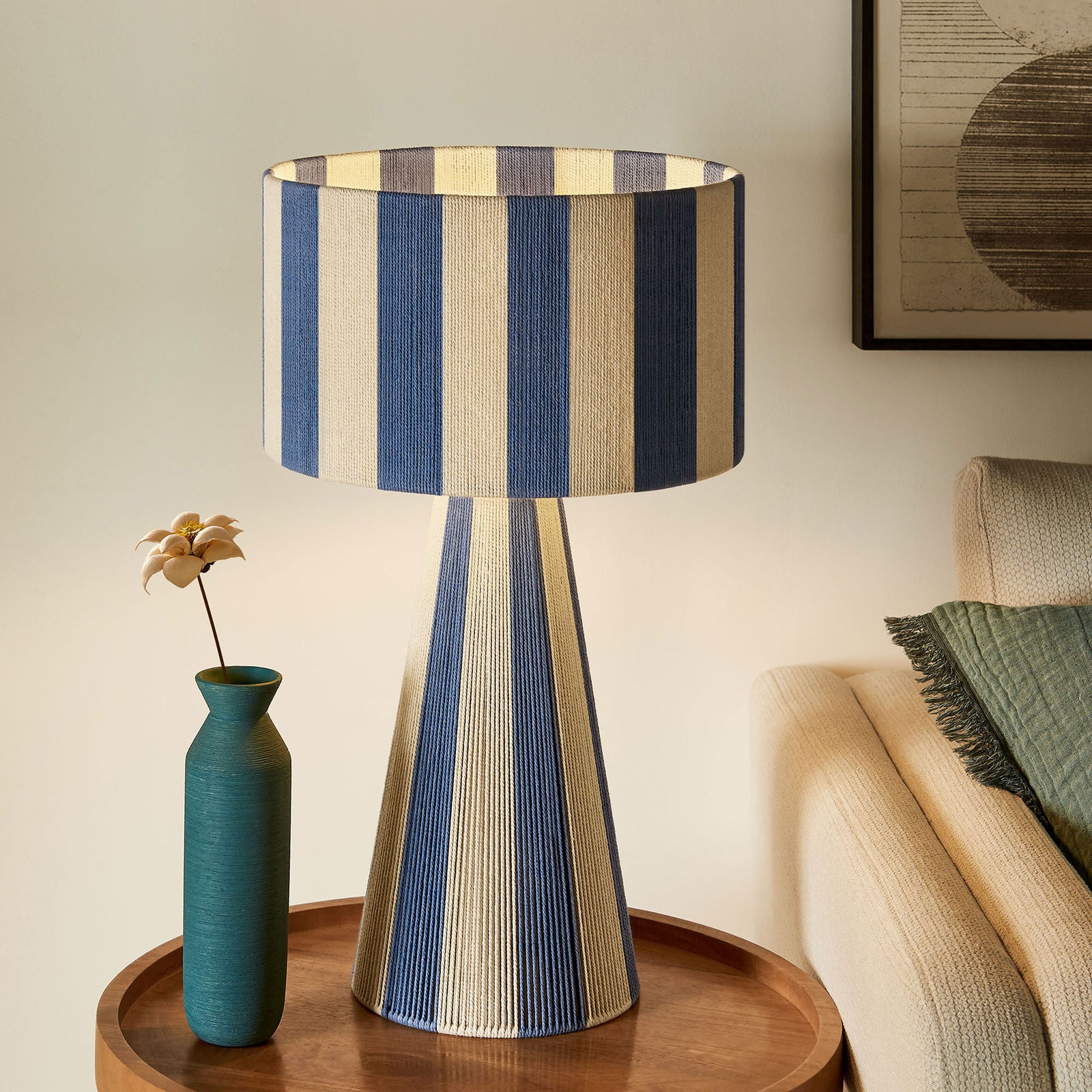 Glowing capri blue striped table lamp brings warm ambient light beside an inviting sofa. || EEI-7261-CBL || front_on_room