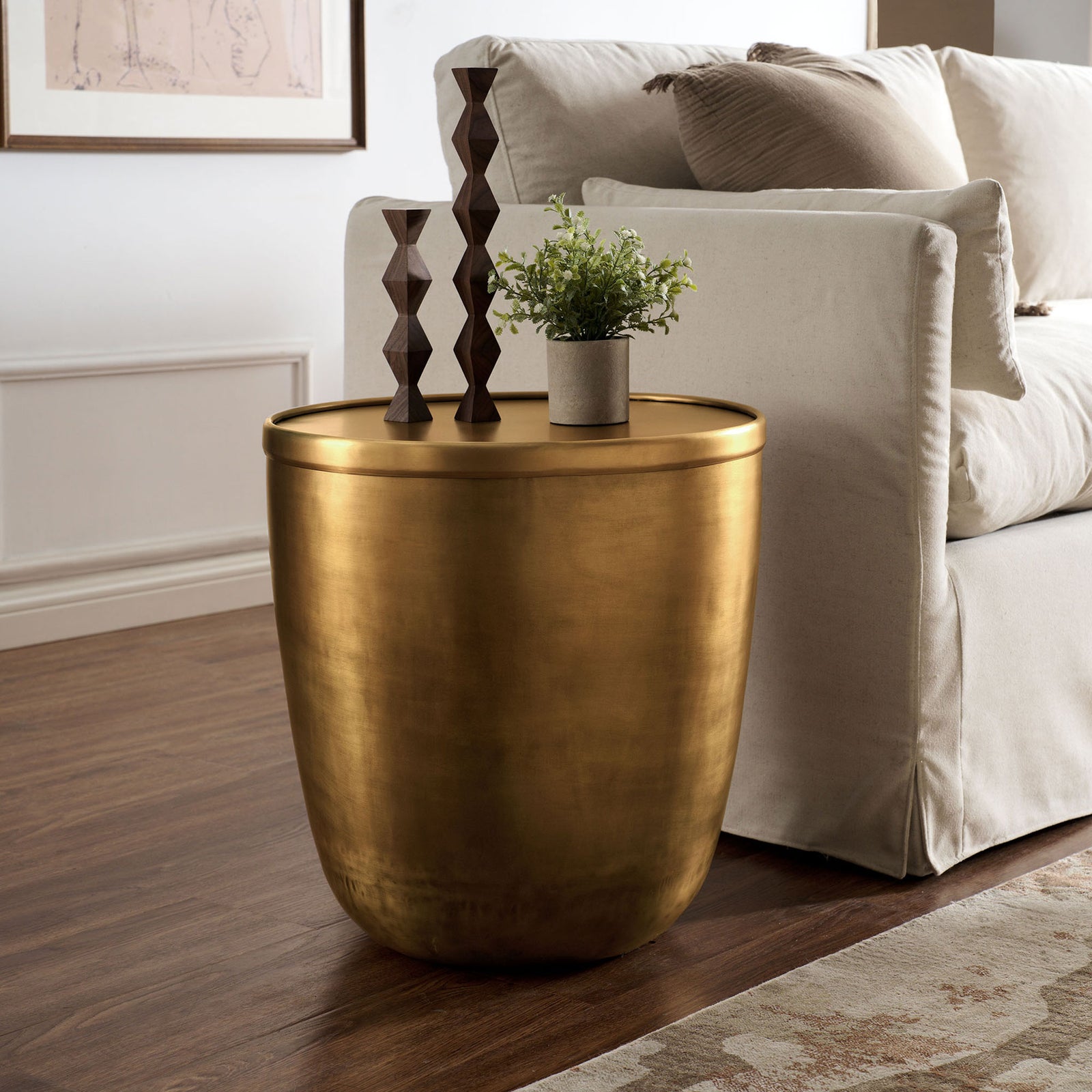 Viora burnished brass drum side table beside a sofa, doubling as a chic accent and drink table. || EEI-7272-BBR || front_angle_room