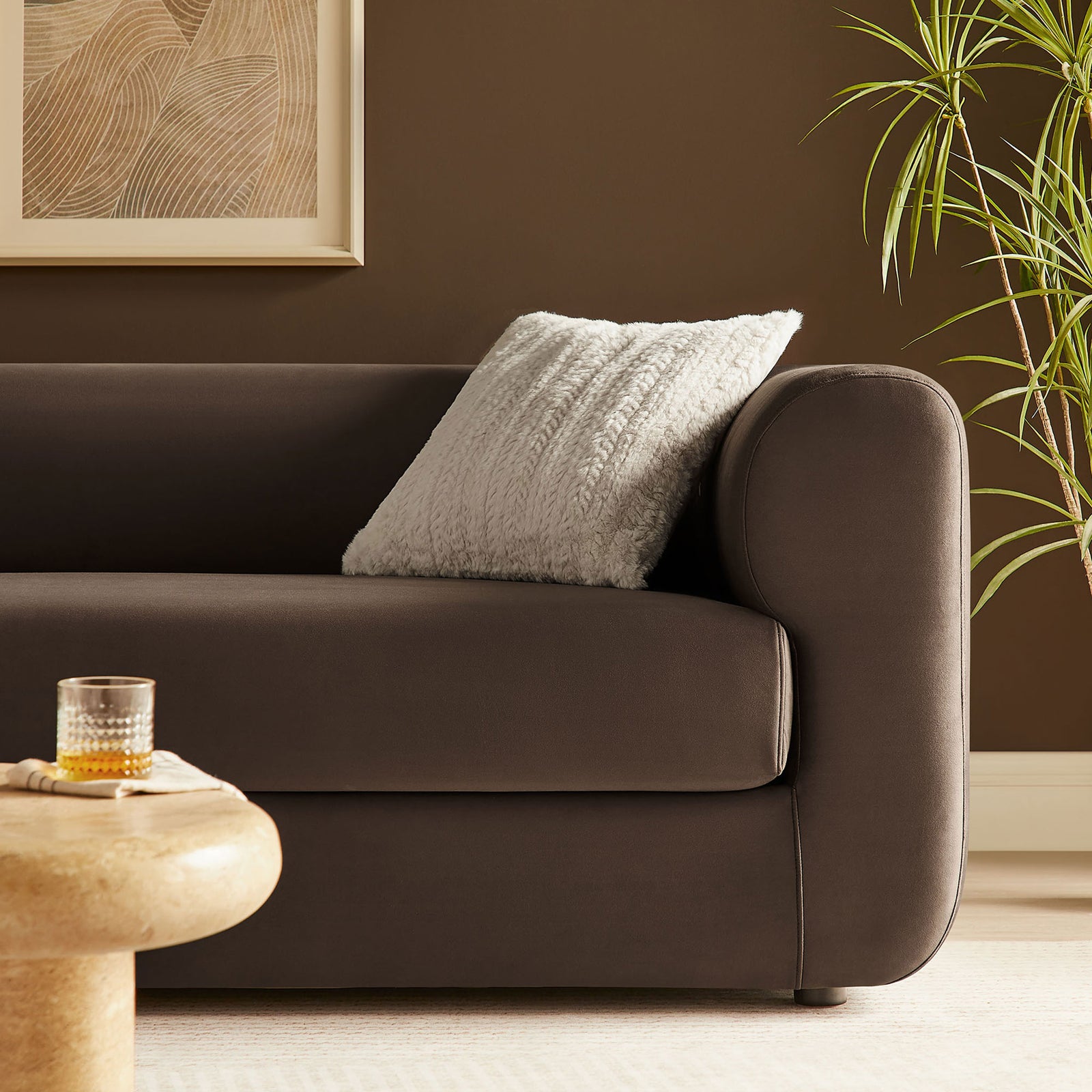Styled chocolate brown velvet sofa arm with textured accent pillow beside a sculptural stone coffee table || EEI-7281-CHB || detail_room