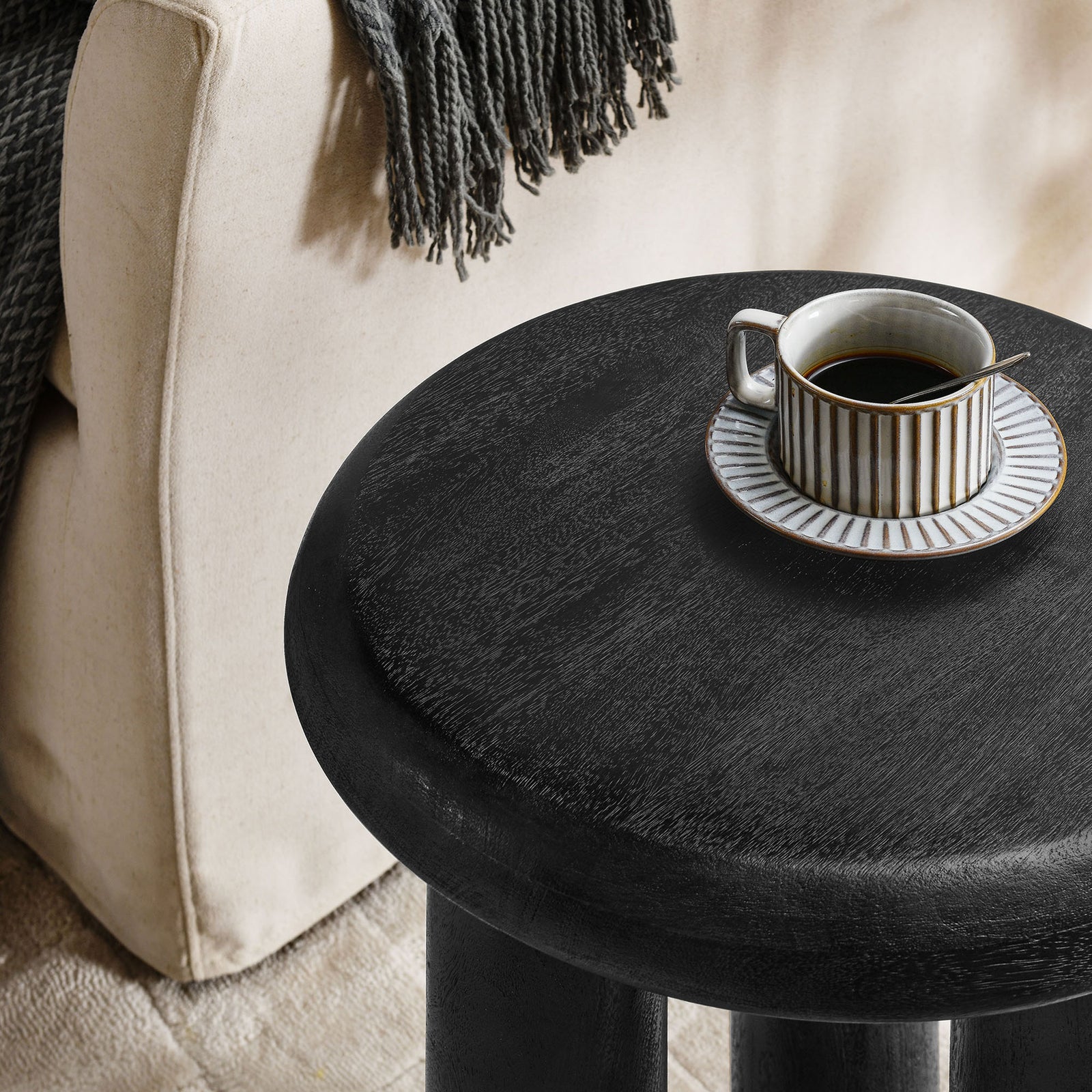 Black mango wood side table beside a sofa styled with a coffee cup on the smooth round top || EEI-7284-BLK || detail_room
